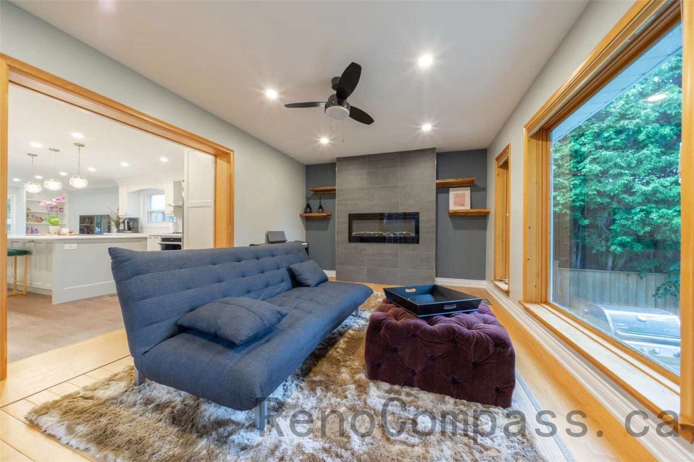 his North York interior renovation features a cozy family room designed with a modern wall-mounted fireplace, large picture windows, and warm wood trim that brings natural light into the space. The layout connects seamlessly to the open-concept kitchen, creating a comfortable environment for family gatherings and everyday living. Completed by a professional Toronto renovation company, the design combines contemporary finishes, recessed lighting, and inviting textures to create a stylish and functional living area.