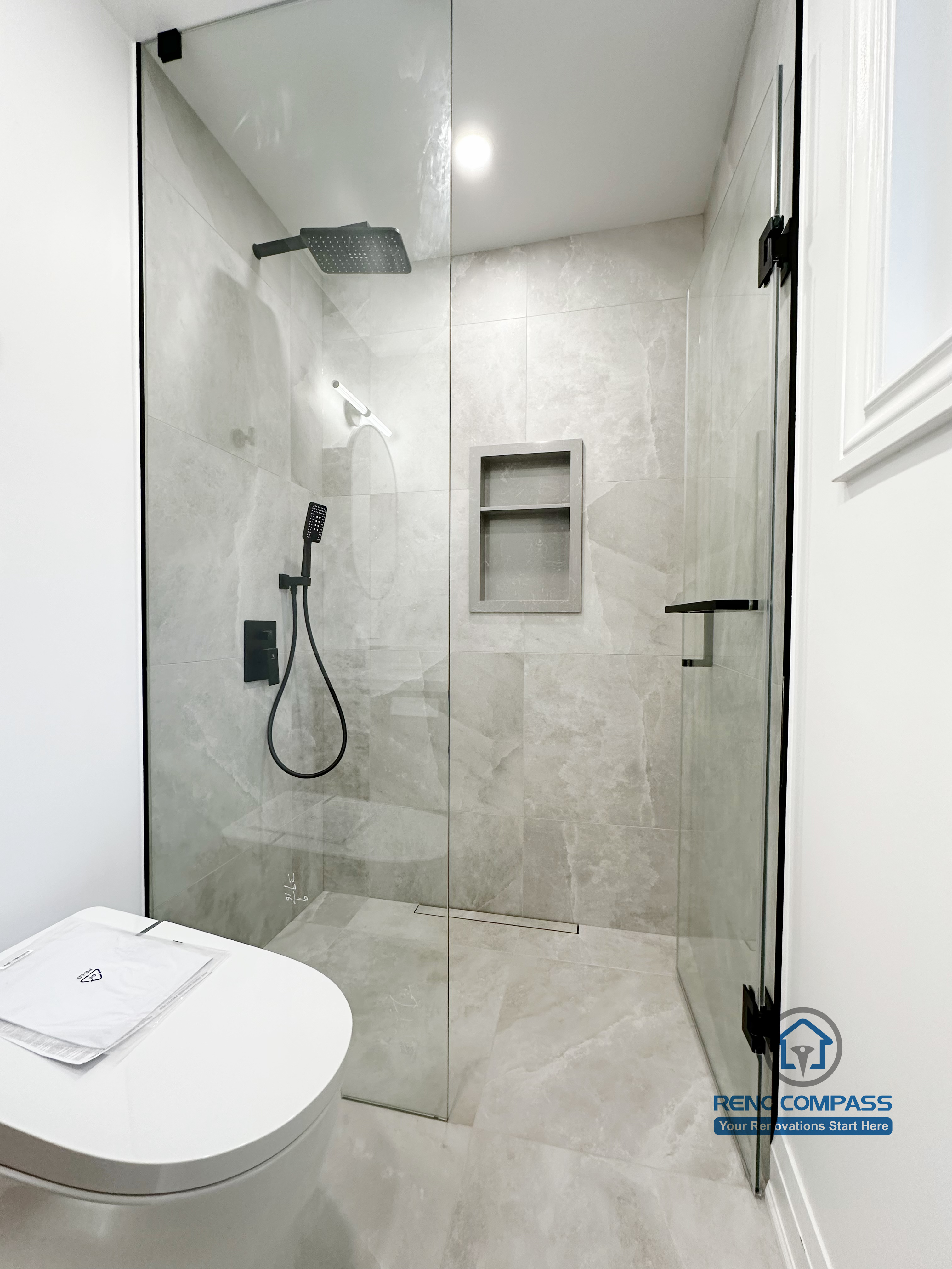 Bathroom renovation in Markham featuring a frameless glass shower with large-format tile, built-in wall niche, matte black shower fixtures, and a clean minimalist layout. The design emphasizes efficient use of space, easy maintenance, and a modern finish.
