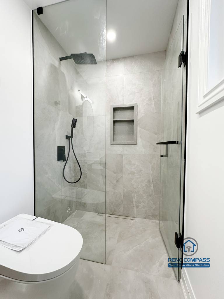 Bathroom renovation in Markham featuring a frameless glass shower with large-format tile, built-in wall niche, matte black shower fixtures, and a clean minimalist layout. The design emphasizes efficient use of space, easy maintenance, and a modern finish.