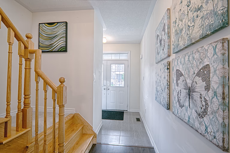 This modern entryway renovation features a bright and welcoming hallway with upgraded tile flooring, a clean neutral color palette, and a beautifully finished wooden staircase with classic railings. Decorative wall art and thoughtful lighting enhance the visual depth of the space while maintaining a contemporary residential aesthetic. Designed to improve both functionality and first impressions, this entrance and staircase upgrade reflects the detail-focused craftsmanship of a trusted Toronto renovation company specializing in full home interior transformations.