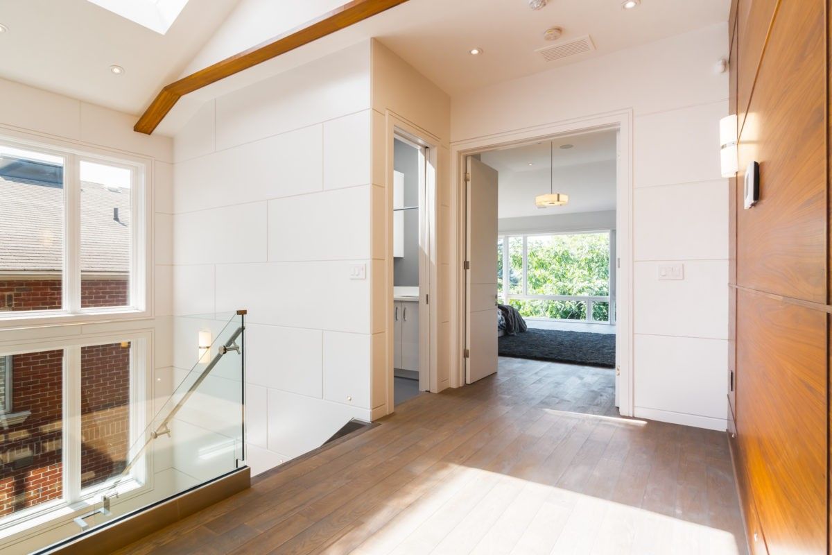 This Toronto modern interior renovation showcases a bright open hallway featuring wide-plank wood flooring, minimalist white wall panels, and a sleek glass stair railing. Natural light flows through large windows, enhancing the clean architectural lines and creating a warm, contemporary living environment.