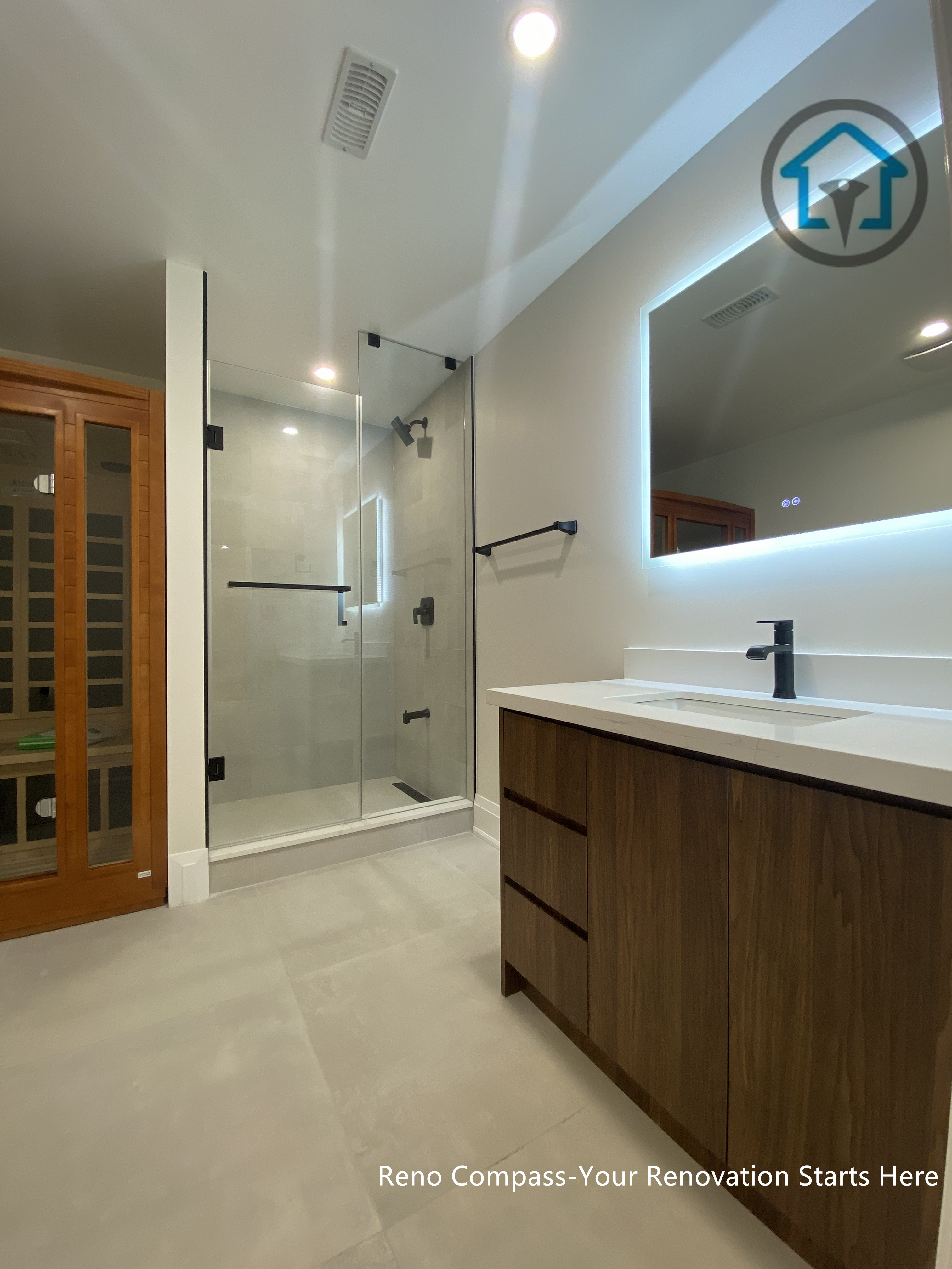 This image features a modern bathroom renovation within a Richmond Hill interior renovation project, showcasing a frameless glass shower, custom wood vanity, and an LED backlit mirror that enhances both functionality and ambiance. Clean tile finishes and minimalist fixtures create a calm, spa-inspired atmosphere designed for everyday comfort. Designed and completed by Reno Compass, this bathroom reflects a refined and practical approach to contemporary bathroom design for homes in Richmond Hill.