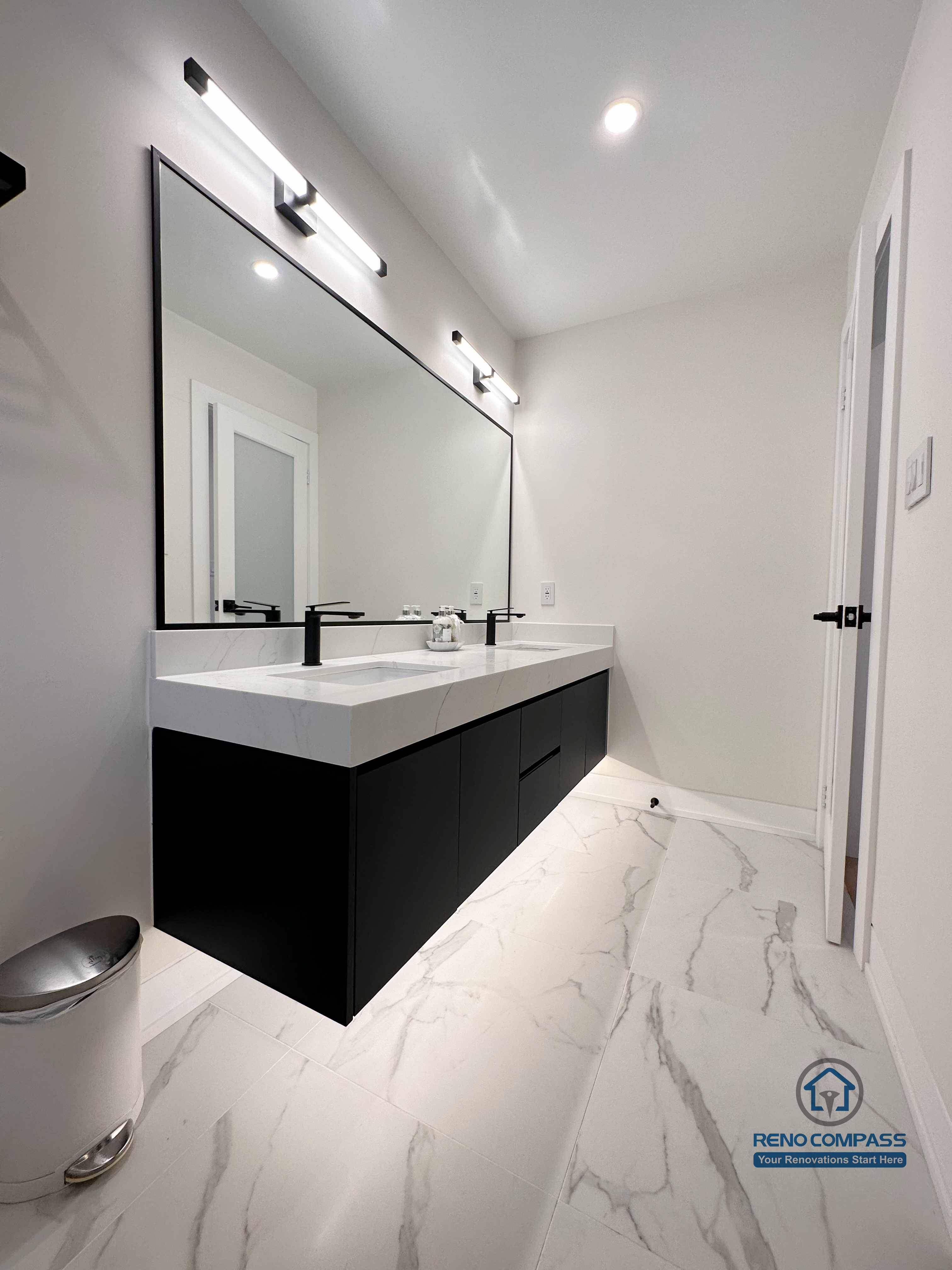 Clean and modern bathroom renovation in Toronto featuring a sleek floating vanity, oversized wall-mounted mirror, contemporary lighting, matte black fixtures, and marble-look porcelain flooring. Completed by a professional Toronto renovation company with a focus on minimalist design and everyday functionality.