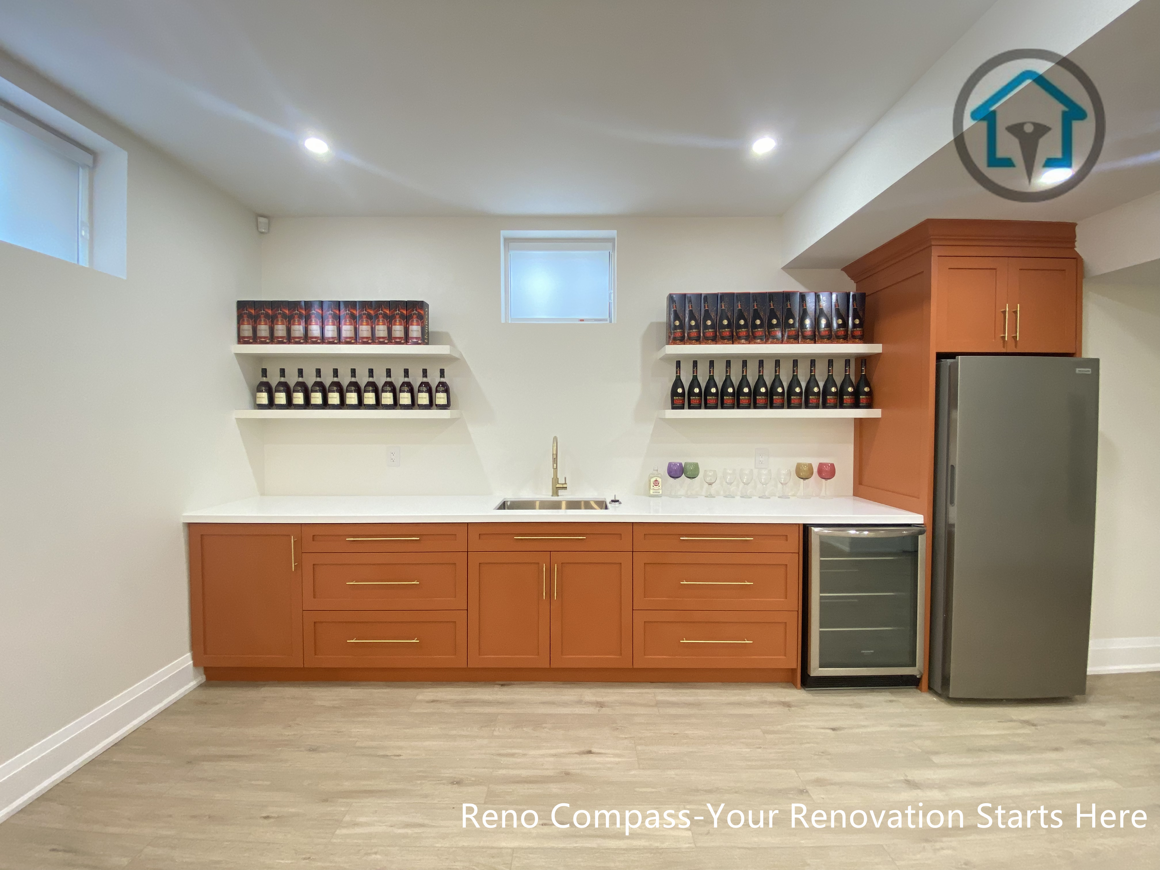 This image showcases a custom basement bar renovation in Richmond Hill, featuring warm-toned cabinetry, integrated wine shelving, a built-in beverage fridge, and a clean quartz countertop with sink. The layout balances storage, display, and functionality, creating a refined entertaining space ideal for hosting and everyday use. Designed and completed by Reno Compass, this basement renovation highlights thoughtful millwork design and practical space planning for modern family living in Richmond Hill.