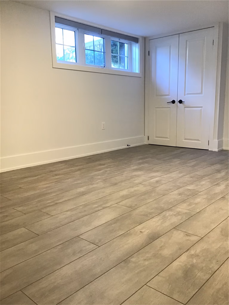 This Markham full home renovation features a clean and modern basement space with durable wood-look vinyl plank flooring, smooth white walls, and newly installed windows for improved natural light. The minimalist design enhances openness and functionality, making the room ideal for multi-purpose use. Completed by a trusted Toronto Renovation Company, this project reflects quality craftsmanship and practical design solutions.