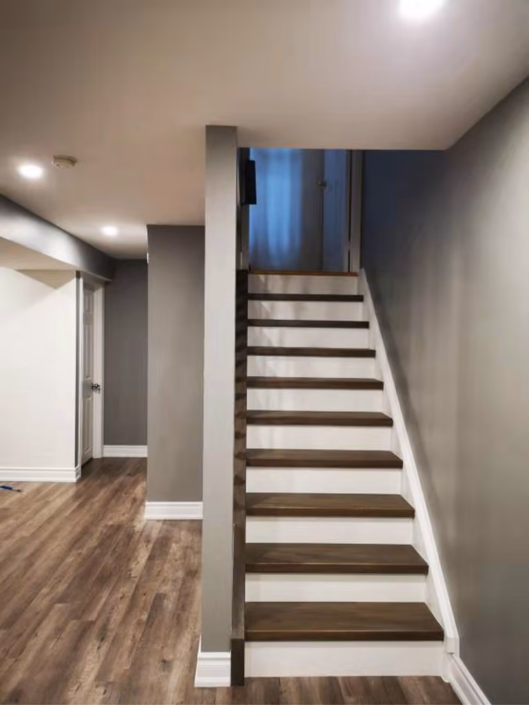 This finished Mississauga basement features a modern staircase with wood treads, white risers, and a clean open design. Paired with upgraded flooring and recessed lighting, the space reflects high-quality craftsmanship by a professional Toronto renovation company, enhancing both safety and contemporary style.