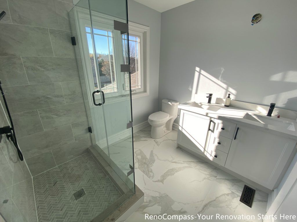 This Thornhill bathroom renovation presents a bright and well-balanced layout featuring a frameless glass walk-in shower, a modern vanity, and a large window that brings in abundant natural light. The herringbone-patterned shower base adds visual texture, while marble-look porcelain flooring enhances continuity throughout the space. Matte black fixtures provide subtle contrast, creating a clean, functional bathroom designed for daily use, comfort, and long-term durability.