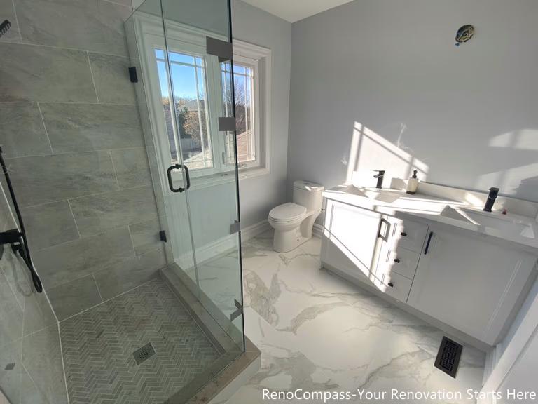 This Thornhill bathroom renovation presents a bright and well-balanced layout featuring a frameless glass walk-in shower, a modern vanity, and a large window that brings in abundant natural light. The herringbone-patterned shower base adds visual texture, while marble-look porcelain flooring enhances continuity throughout the space. Matte black fixtures provide subtle contrast, creating a clean, functional bathroom designed for daily use, comfort, and long-term durability.