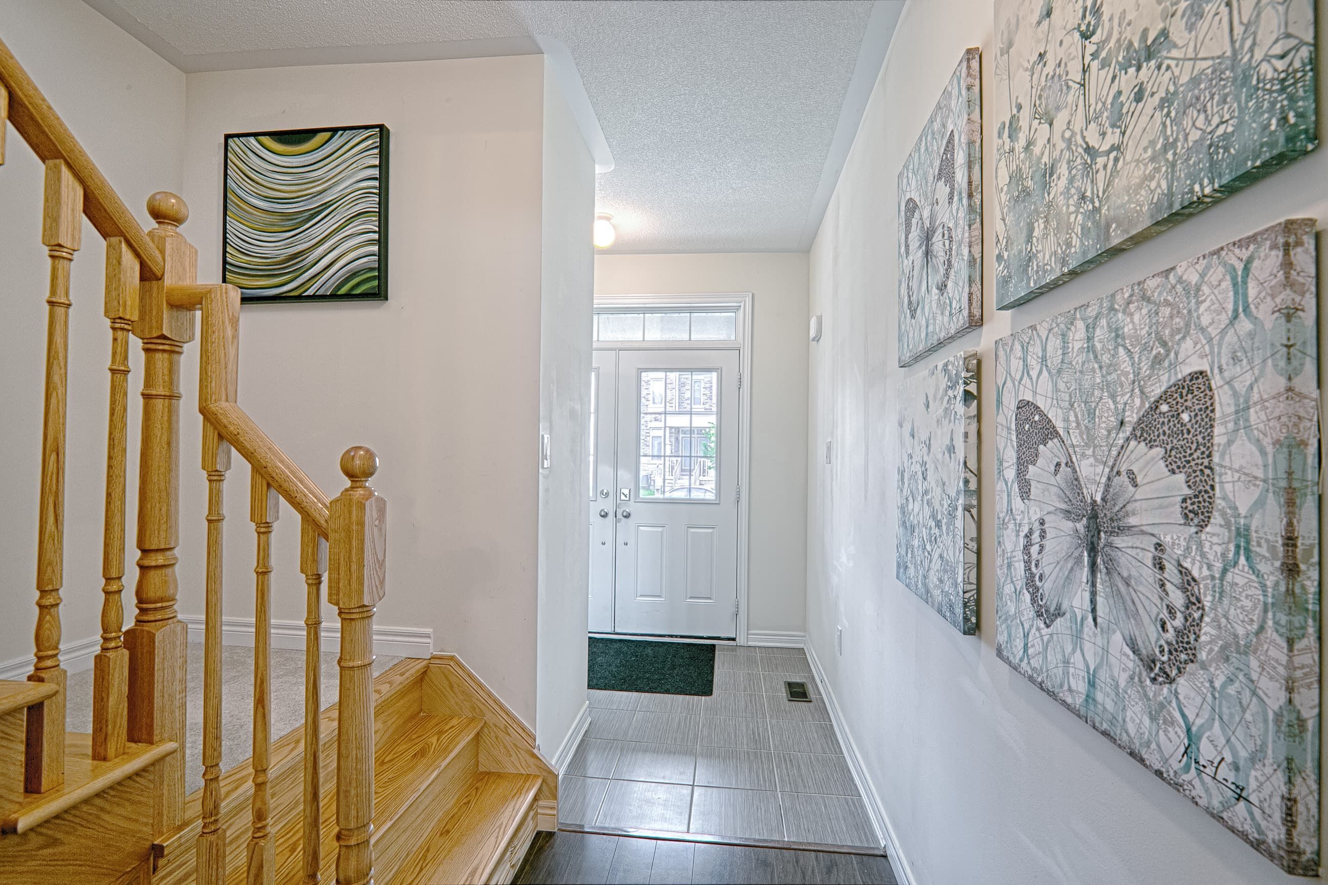 This modern entryway renovation features a bright and welcoming hallway with upgraded tile flooring, a clean neutral color palette, and a beautifully finished wooden staircase with classic railings. Decorative wall art and thoughtful lighting enhance the visual depth of the space while maintaining a contemporary residential aesthetic. Designed to improve both functionality and first impressions, this entrance and staircase upgrade reflects the detail-focused craftsmanship of a trusted Toronto renovation company specializing in full home interior transformations.