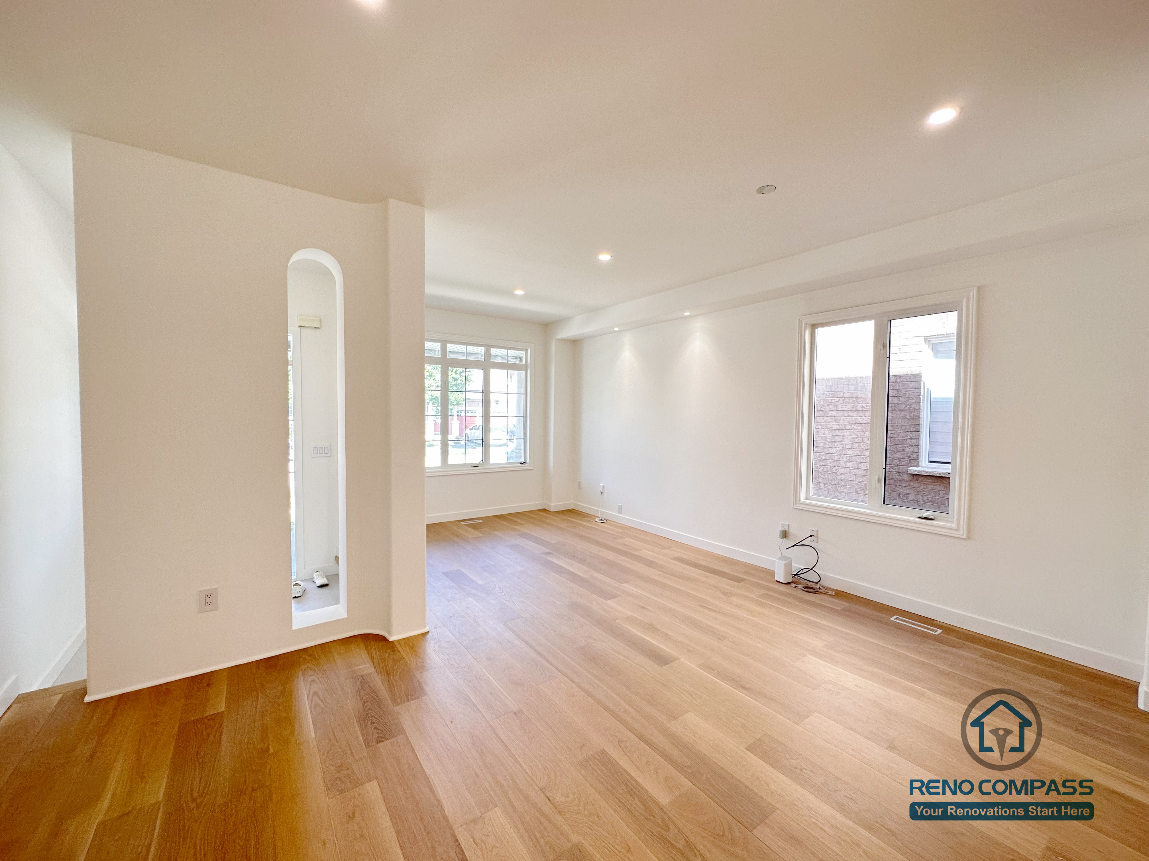 This image features a Markham flooring renovation showcasing wide-plank hardwood floors in a bright, open living area. The continuous wood flooring, recessed ceiling lights, and clean wall lines enhance natural light and create a spacious, modern atmosphere. Large windows and simple architectural details emphasize balance and everyday livability. Completed by a professional Toronto renovation company, Reno Compass Inc., this flooring project prioritizes durability, visual warmth, and long-term residential comfort.