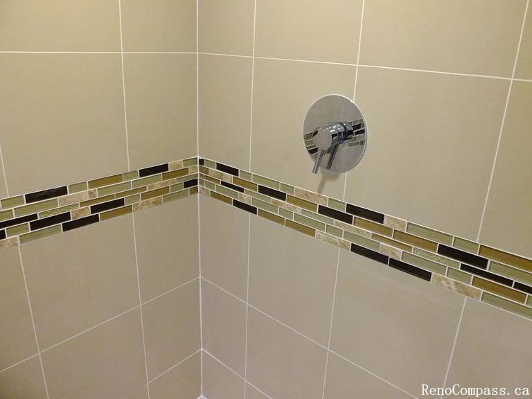 This Mississauga bathroom renovation highlights a clean and modern shower wall design featuring large-format beige tiles paired with a decorative mosaic accent strip. The horizontal mosaic band adds visual interest and depth while maintaining a balanced, neutral color palette. The chrome shower control fixture complements the tile work and provides a sleek, contemporary finish. This detail-focused installation demonstrates quality craftsmanship and thoughtful design, enhancing both the style and durability of the bathroom space.