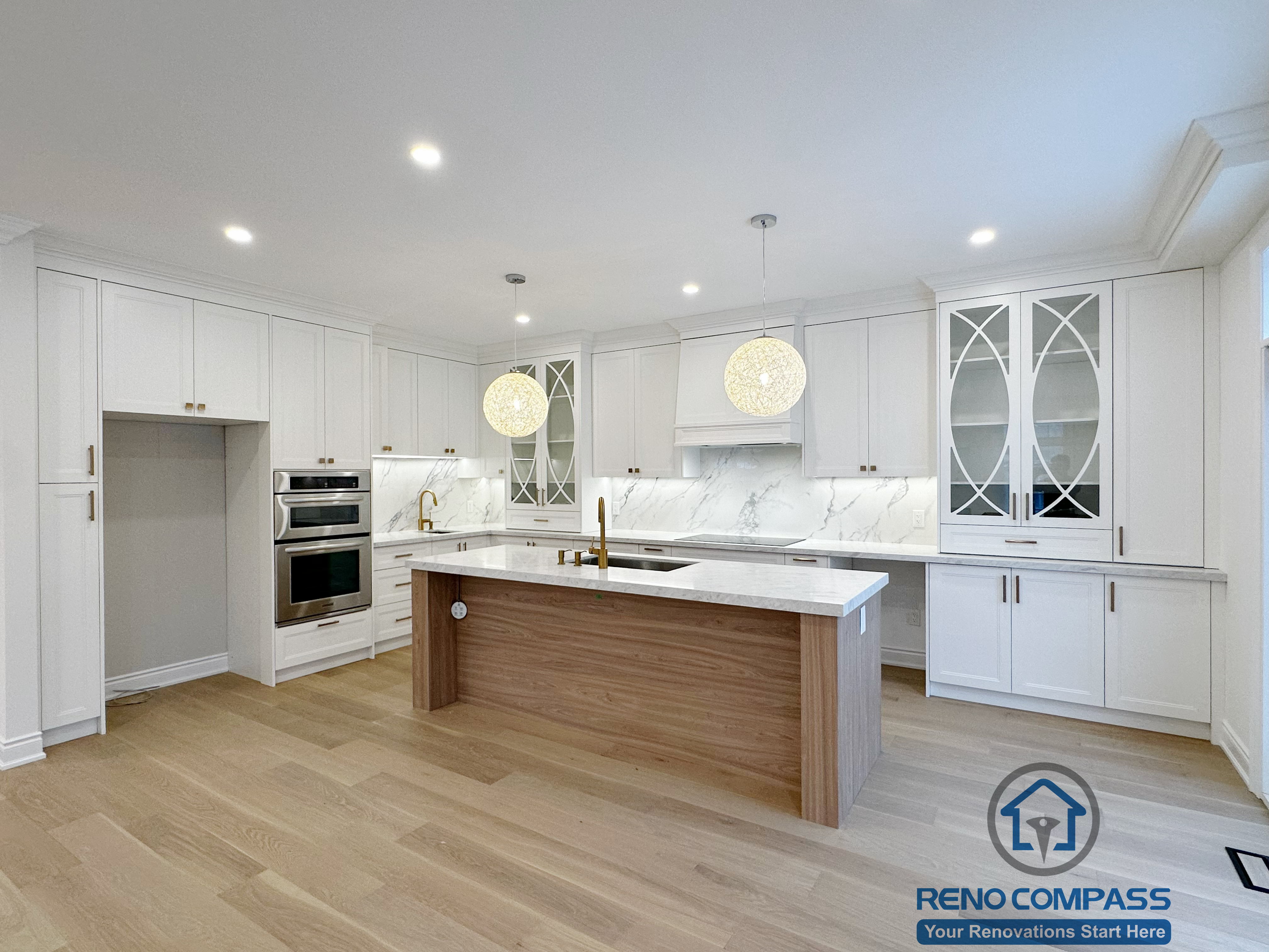 Bright and elegant Vaughan interior renovation featuring a custom white kitchen, waterfall island with wood paneling, marble-look backsplash, built-in appliances, and light hardwood flooring. This modern space showcases clean lines, functional layout, and high-end craftsmanship by a professional Toronto renovation company.