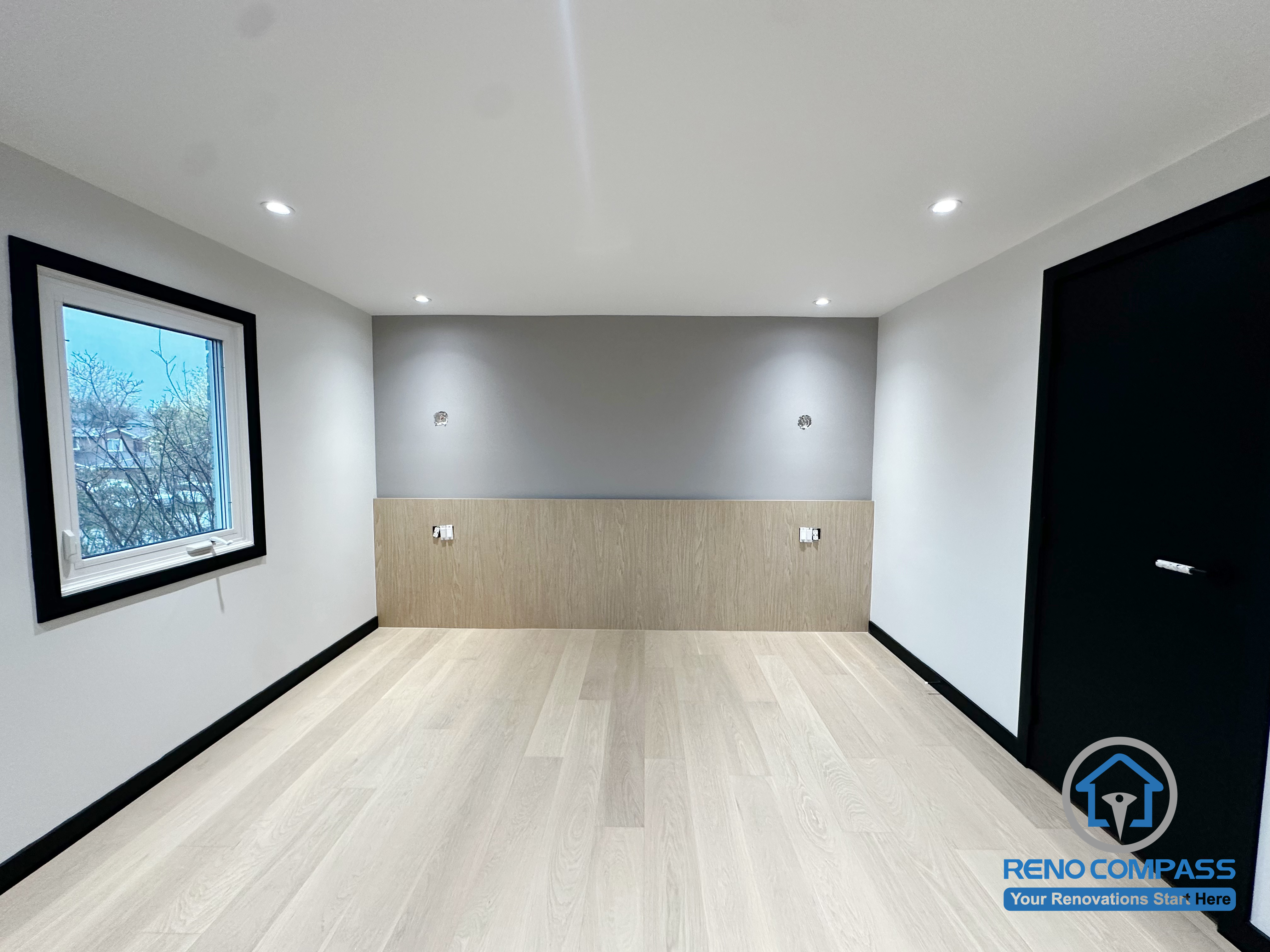 This bedroom in Richmond Hill features a clean modern upgrade with a soft grey accent wall and custom wood paneling. The minimalist design improves warmth, storage possibilities, and overall comfort. A bright window and balanced lighting further enhance the peaceful atmosphere. 这间位于列治文山的卧室经过现代化升级，以柔和的灰色特色墙搭配温润的木纹护墙板，让空间更显温暖与质感。极简设计提升了整体舒适度，明亮窗户与均匀灯光营造出宁静、放松的休息氛围。