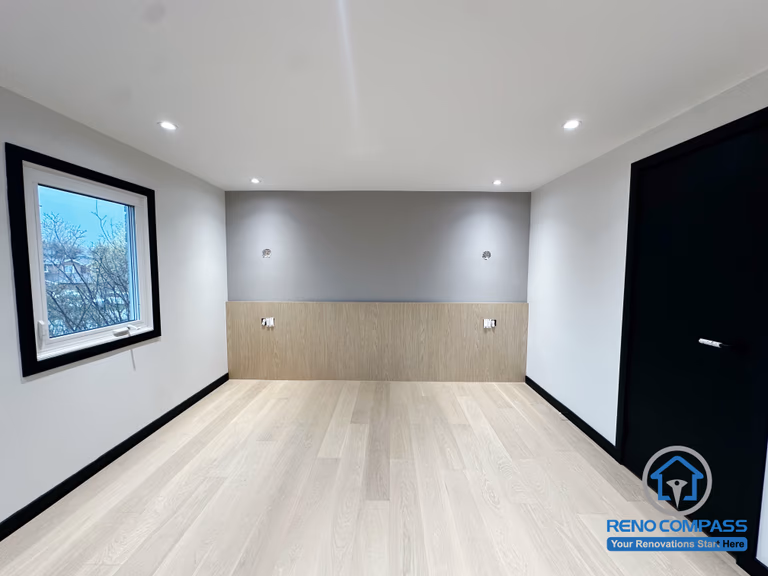 This bedroom in Richmond Hill features a clean modern upgrade with a soft grey accent wall and custom wood paneling. The minimalist design improves warmth, storage possibilities, and overall comfort. A bright window and balanced lighting further enhance the peaceful atmosphere. 这间位于列治文山的卧室经过现代化升级，以柔和的灰色特色墙搭配温润的木纹护墙板，让空间更显温暖与质感。极简设计提升了整体舒适度，明亮窗户与均匀灯光营造出宁静、放松的休息氛围。