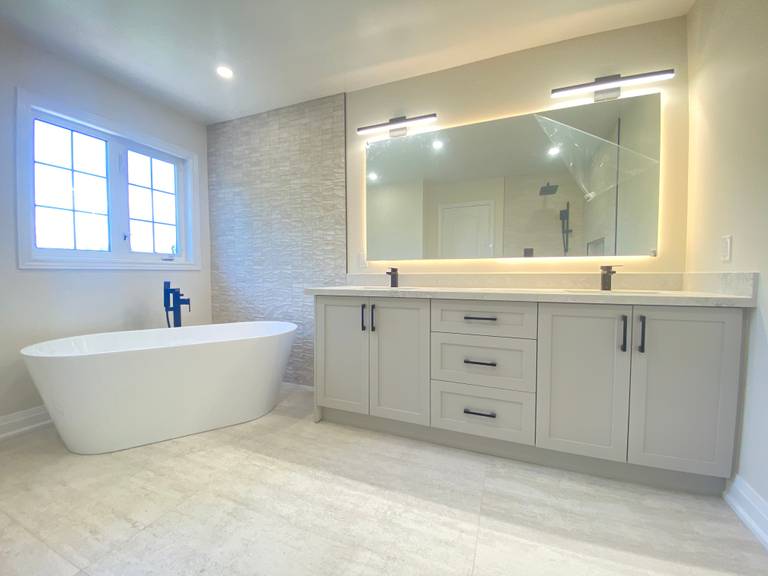 A spacious master bathroom completed as part of a Richmond Hill interior renovation. This bathroom renovation features a freestanding soaking tub, custom double vanity with integrated storage, LED backlit mirror lighting, large-format floor tiles, and matte black fixtures for a clean, modern finish.