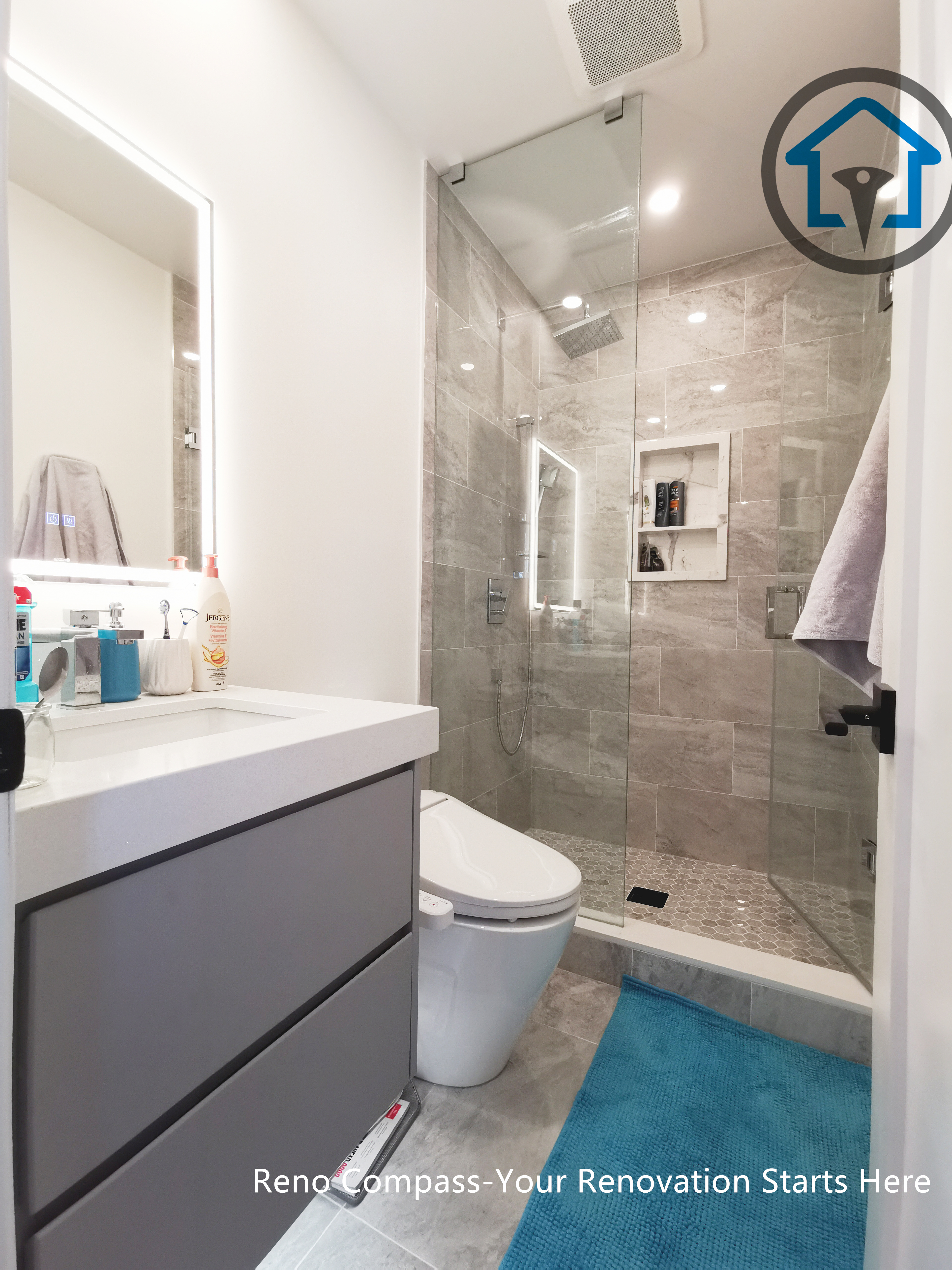 This North York bathroom renovation features a modern floating-style vanity paired with a quartz countertop and a glass-enclosed shower. Neutral wall tiles, built-in shower storage, and LED mirror lighting create a clean and functional layout that maximizes space and comfort. Completed by a Toronto renovation company focused on efficient bathroom design and quality craftsmanship.