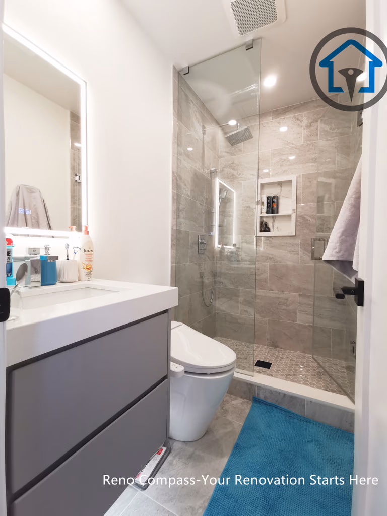 This North York bathroom renovation features a modern floating-style vanity paired with a quartz countertop and a glass-enclosed shower. Neutral wall tiles, built-in shower storage, and LED mirror lighting create a clean and functional layout that maximizes space and comfort. Completed by a Toronto renovation company focused on efficient bathroom design and quality craftsmanship.