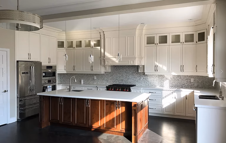 This modern Markham kitchen renovation features custom white cabinetry, a large central island with dark wood base, quartz countertops, and built-in stainless steel appliances. Elegant mosaic backsplash, detailed crown molding, and pendant lighting create a bright and luxurious cooking space. Completed by a professional Toronto renovation company, this kitchen combines functionality, storage, and timeless design for modern family living.