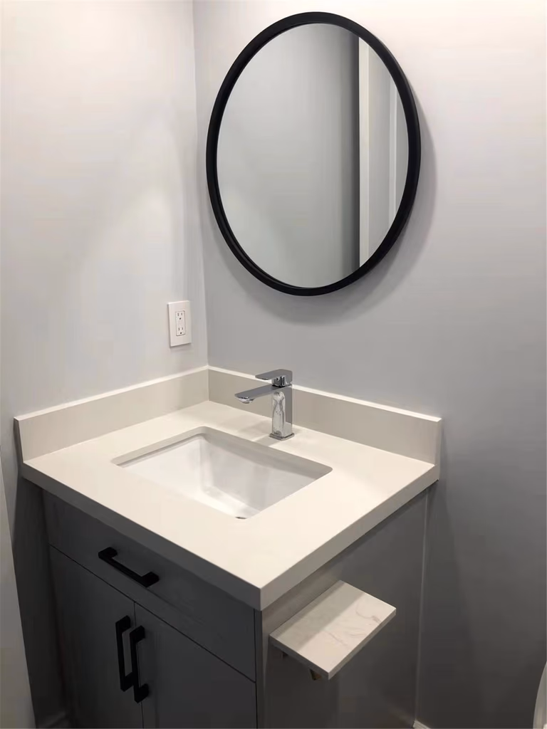This Richmond Hill bathroom renovation highlights a modern vanity with quartz countertop, integrated sink, and sleek black hardware paired with a minimalist round mirror. The clean layout maximizes space while maintaining a bright and contemporary look. Completed by a professional Toronto renovation company, this upgrade delivers functional storage, durable finishes, and a timeless bathroom design suitable for everyday use.