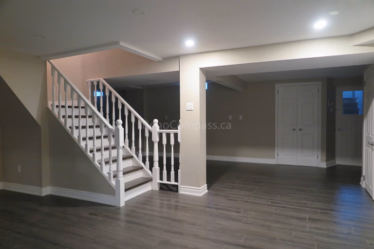 This Markham basement renovation features a spacious open-concept layout with newly installed modern flooring, fresh neutral paint, and upgraded staircase with white railings and trim detailing. Recessed LED lighting enhances brightness throughout the lower level, creating a functional and welcoming space ideal for a family lounge, recreation area, or rental suite potential. Completed by Reno Compass, a professional renovation contractor delivering high-quality basement finishing and interior renovation services across Markham and the Greater Toronto Area.