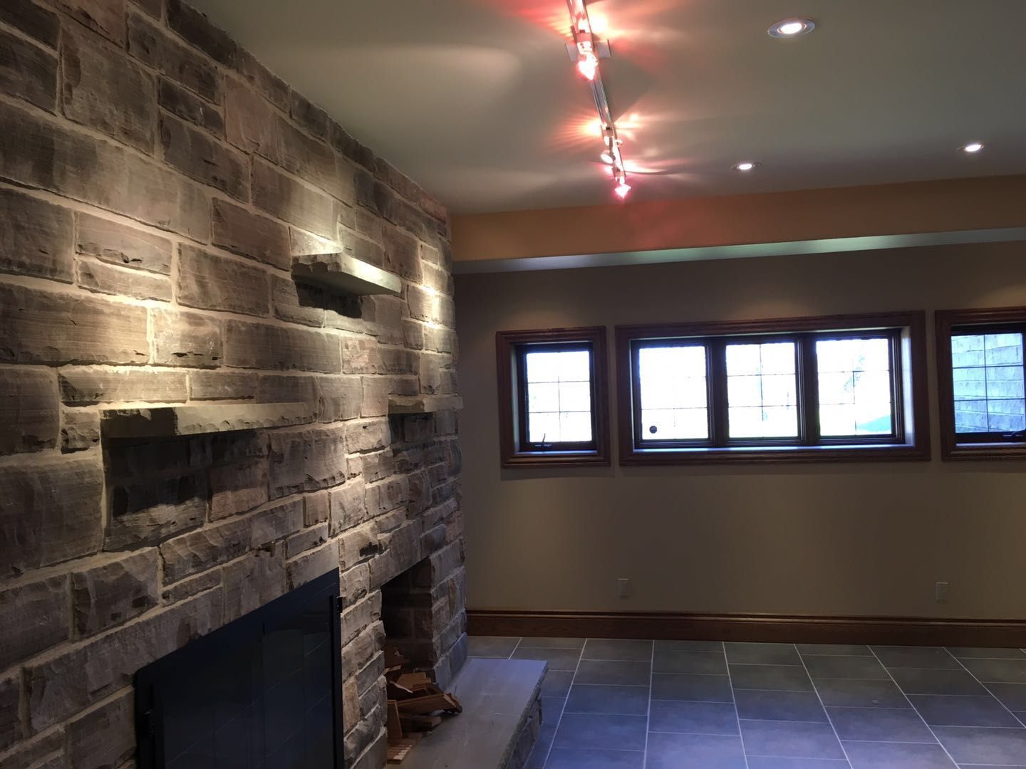 This Toronto interior renovation showcases a spacious open-concept living area designed with modern large-format tile flooring, warm neutral wall tones, and elegant recessed lighting throughout the ceiling. A beautifully crafted stone fireplace feature wall creates a strong focal point, adding both warmth and architectural character to the space. The upgraded lighting layout enhances brightness and visual depth, making the area ideal for entertaining and everyday living. Completed by a professional Toronto renovation company, this project highlights quality finishes, clean design lines, and a refined contemporary interior transformation.