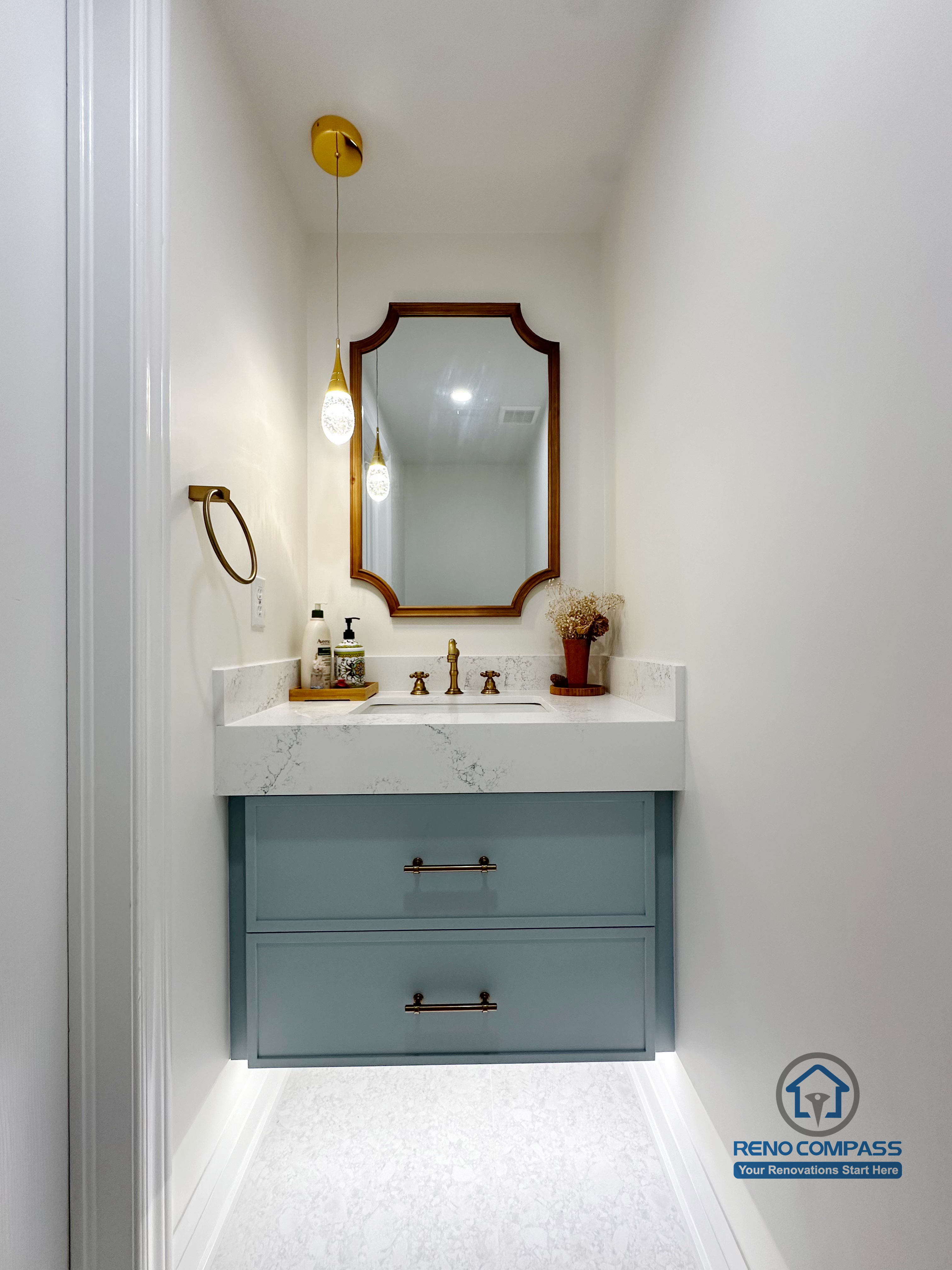 This compact powder room renovation in Markham features a custom blue vanity with quartz countertop, paired with a decorative framed mirror and warm brass fixtures. Soft pendant lighting and clean white walls create a refined, boutique-style atmosphere while maximizing visual depth in a narrow layout. Designed for both functionality and elegance, this space showcases thoughtful proportions, custom cabinetry, and timeless finishes, completed by a professional Toronto-area renovation contractor.