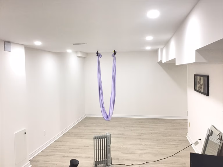 This Aurora basement renovation features a dedicated home gym and wellness area with an open and minimalist layout. The space includes a treadmill, aerial yoga setup, and wide plank flooring, enhanced by recessed ceiling lights for a bright and comfortable workout environment.