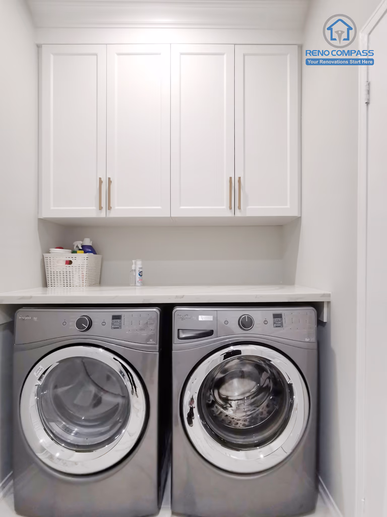 This Markham interior renovation includes a clean and highly functional custom laundry room designed to maximize efficiency within a compact footprint. The space features stacked front-load washer and dryer units integrated beneath custom white shaker cabinetry, providing concealed storage for daily household essentials. A seamless countertop offers a practical folding and sorting surface, while neutral finishes maintain visual continuity with the rest of the home. The streamlined layout improves circulation and ease of use without sacrificing storage capacity. Completed by Reno Compass, this laundry room renovation reflects a thoughtful approach to interior planning, balancing practicality, durability, and a cohesive modern aesthetic suited for Markham residences.