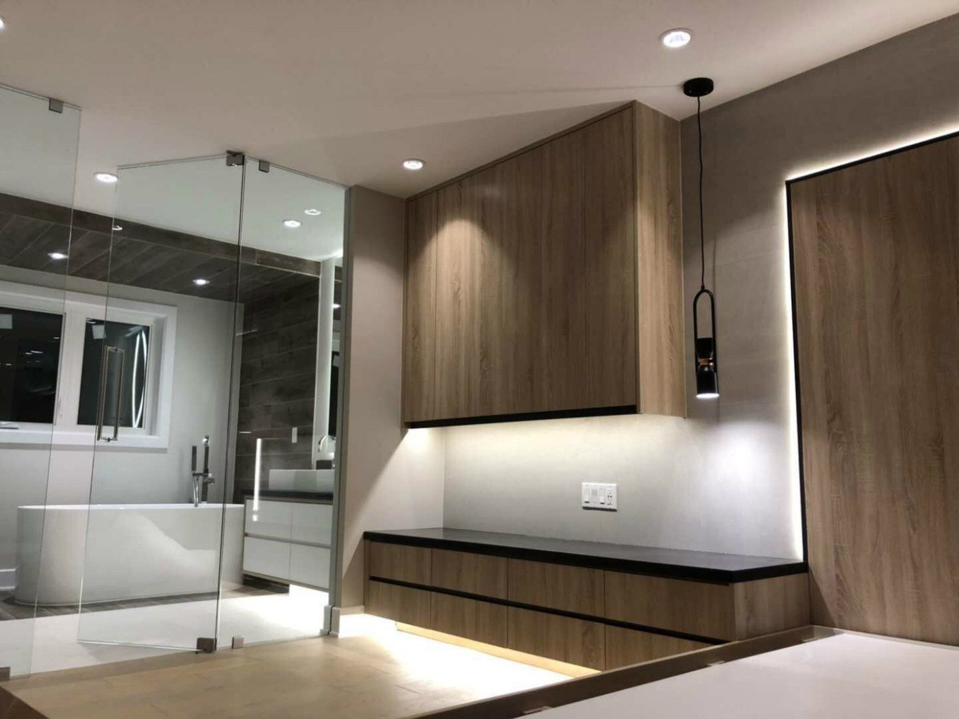 Stylish Markham home renovation featuring custom built-in cabinetry, floating storage, and warm wood panel finishes with integrated LED lighting. The space is enhanced by sleek glass partitions connecting the bedroom and luxury bathroom, creating a seamless, contemporary layout that balances functionality, comfort, and modern interior elegance.