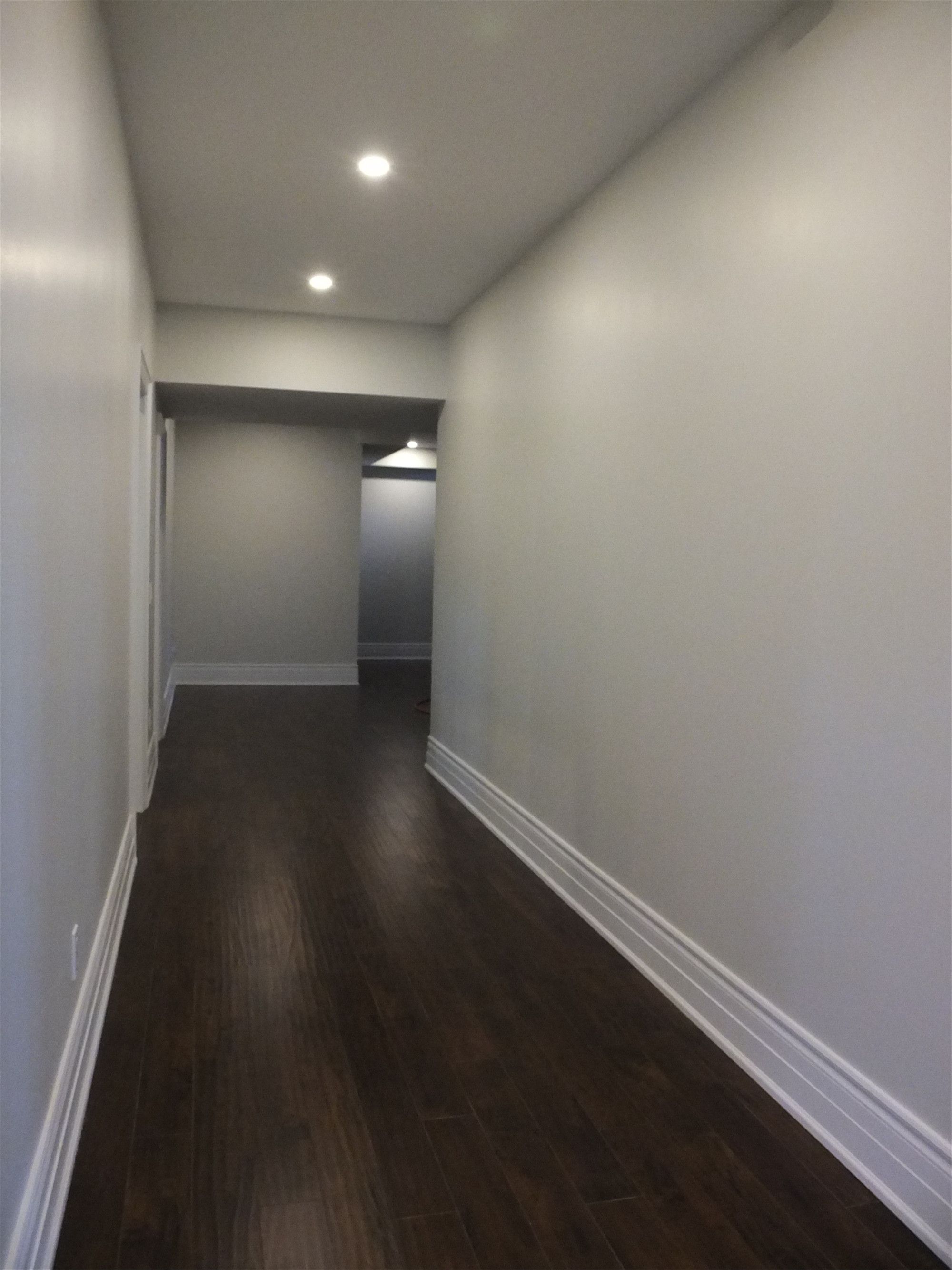 This Richmond Hill basement renovation showcases a clean and modern hallway design featuring recessed pot lights, smooth painted walls, and dark hardwood flooring. The extended corridor layout improves space flow and connects different functional areas within the basement efficiently.