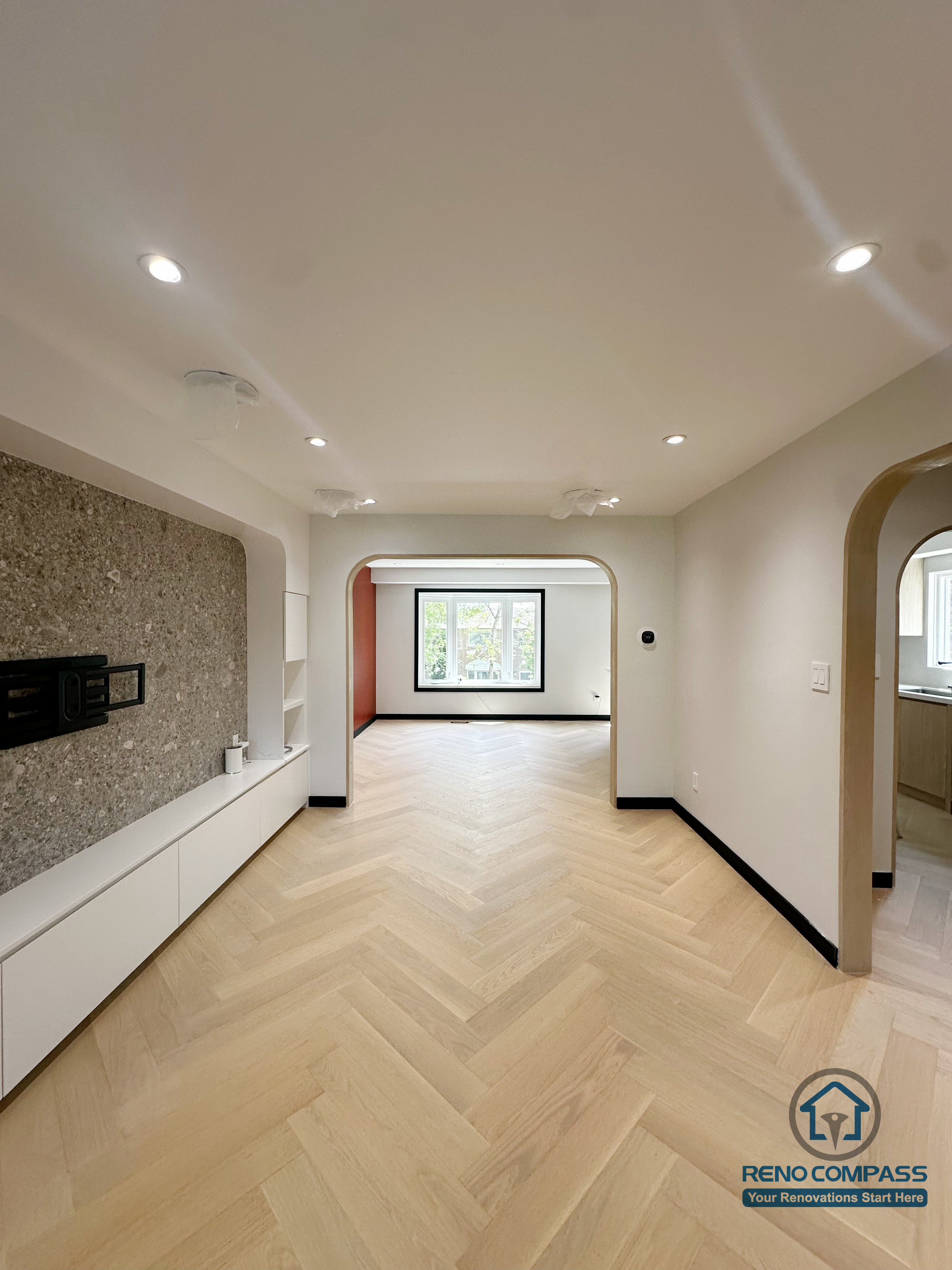 This Richmond Hill open-concept living space was transformed with modern archway details, a custom stone-texture feature wall, and light wood herringbone flooring. The new layout enhances natural light, improves traffic flow, and creates a warm, contemporary living environment—showcasing a clean and timeless renovation style. 这个位于 Richmond Hill 的开放式客厅经过全面升级，保留原有格局的基础上加入了弧形拱门、浅木地板与石纹电视背景墙，让空间更柔和、更有设计层次。自然采光被最大化利用，动线更加通透，整体风格现代又温暖，是非常典型的当代住宅翻新案例。