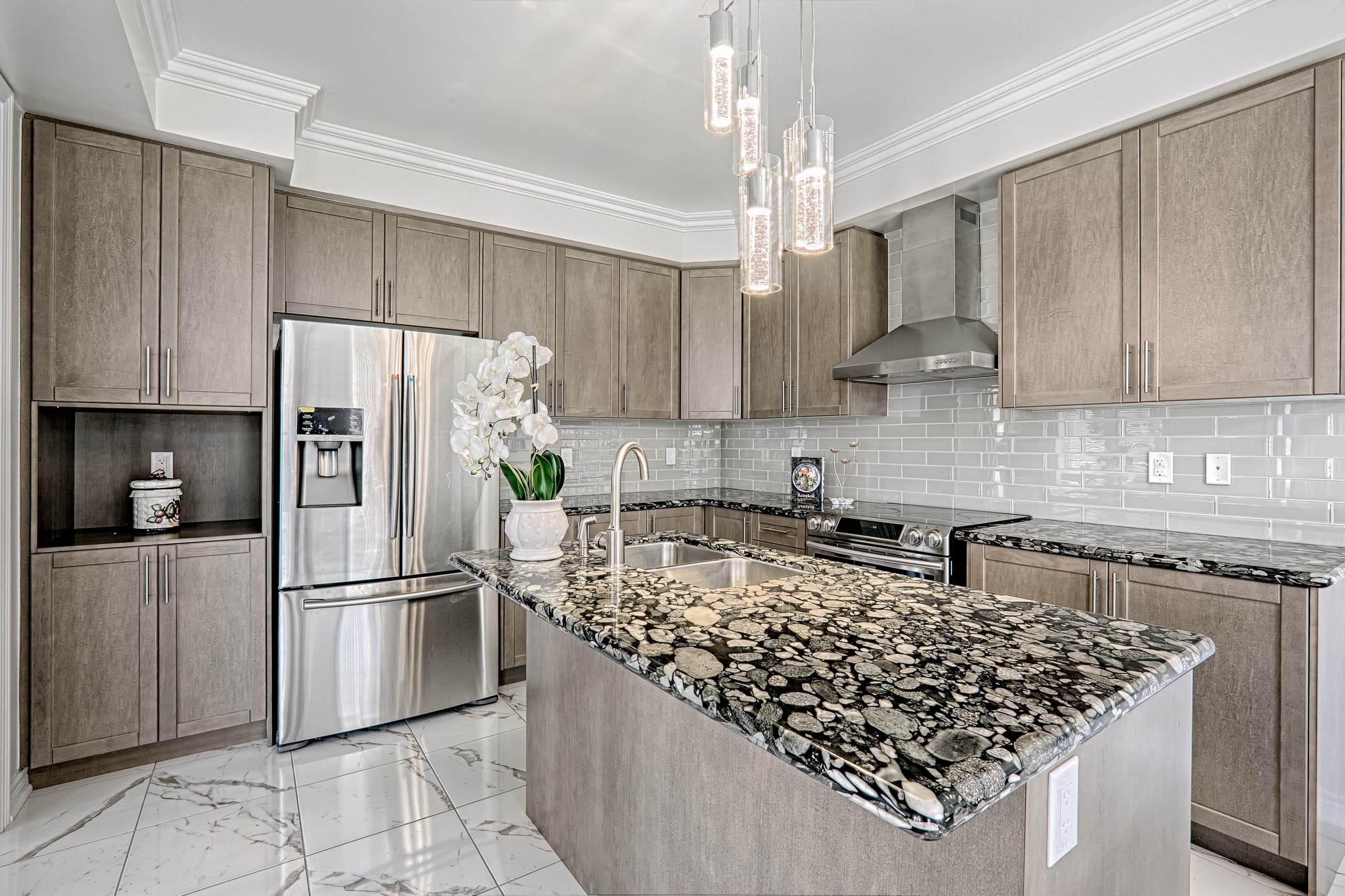 This Toronto luxury kitchen renovation features custom cabinetry, a premium stone waterfall island, and modern stainless steel appliances that create a functional and stylish cooking space. The design highlights elegant pendant lighting, full-height cabinets, and marble-style flooring that enhance both aesthetics and usability. Completed by a professional Toronto renovation company, this modern kitchen project showcases high-end materials, expert craftsmanship, and a bright open-concept layout ideal for contemporary family living.