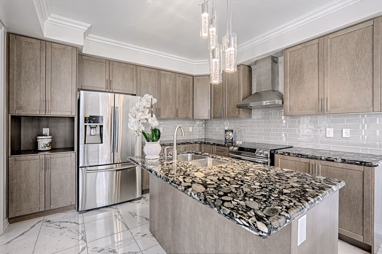 This Toronto luxury kitchen renovation features custom cabinetry, a premium stone waterfall island, and modern stainless steel appliances that create a functional and stylish cooking space. The design highlights elegant pendant lighting, full-height cabinets, and marble-style flooring that enhance both aesthetics and usability. Completed by a professional Toronto renovation company, this modern kitchen project showcases high-end materials, expert craftsmanship, and a bright open-concept layout ideal for contemporary family living.