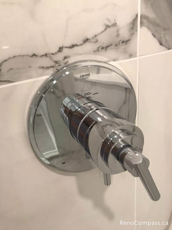 This Markham bathroom renovation detail features a sleek chrome shower control valve installed on elegant marble-pattern porcelain wall tiles. The minimalist fixture design complements the modern shower space, providing precise water temperature control while enhancing the overall clean and contemporary bathroom aesthetic.