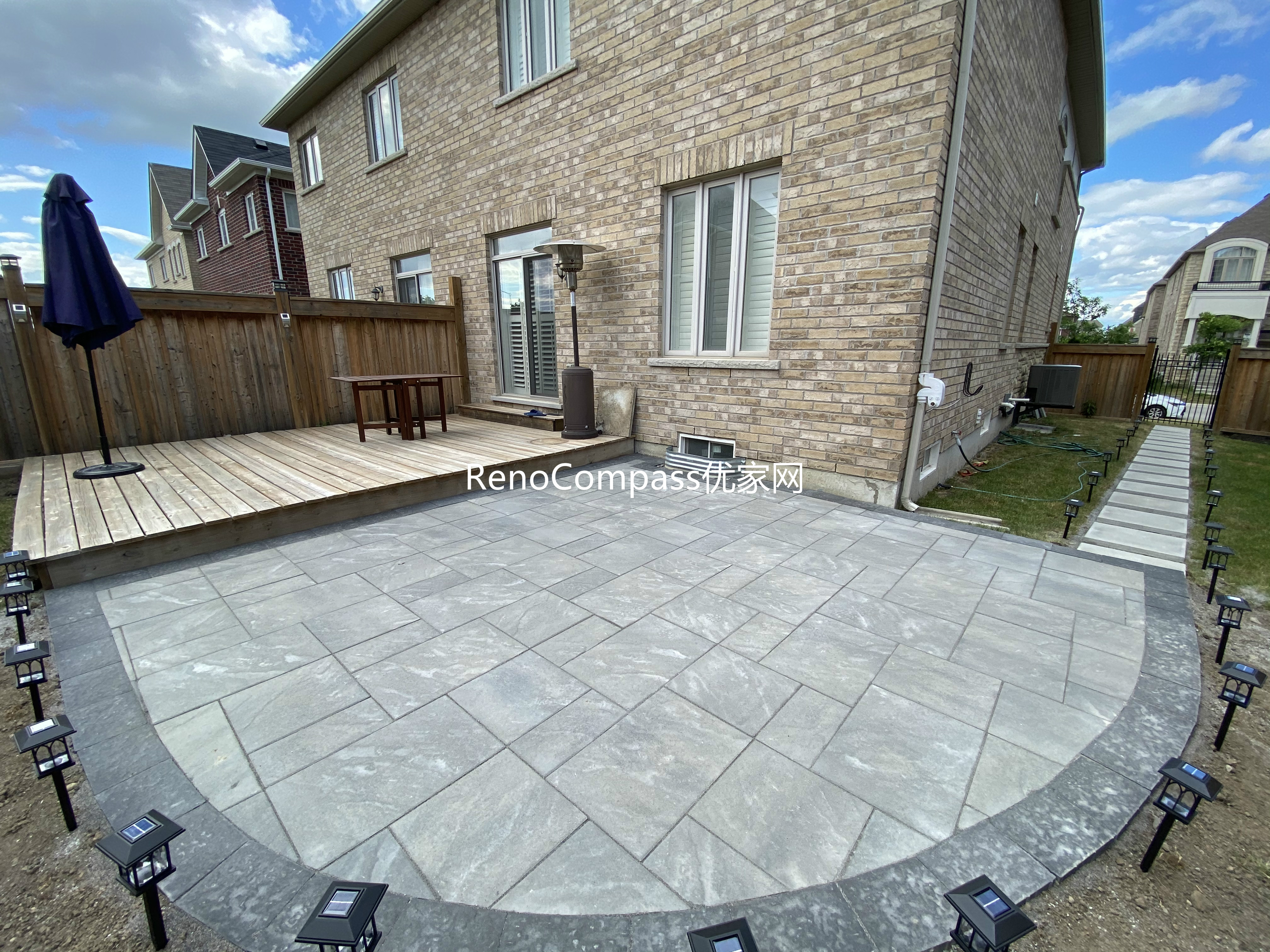 This Markham landscaping and interlocking project features a custom stone patio designed with a curved edge layout to soften the backyard space and improve flow. Large-format interlocking pavers were installed with precise alignment, creating a durable and visually balanced outdoor surface suitable for seating and everyday use. Integrated pathway lighting enhances safety and nighttime visibility, while the patio connects seamlessly with the existing wooden deck and side walkway. The combination of clean stone patterns and thoughtful layout delivers a functional, low-maintenance backyard upgrade completed by Reno Compass, serving homeowners in Markham and the surrounding GTA.