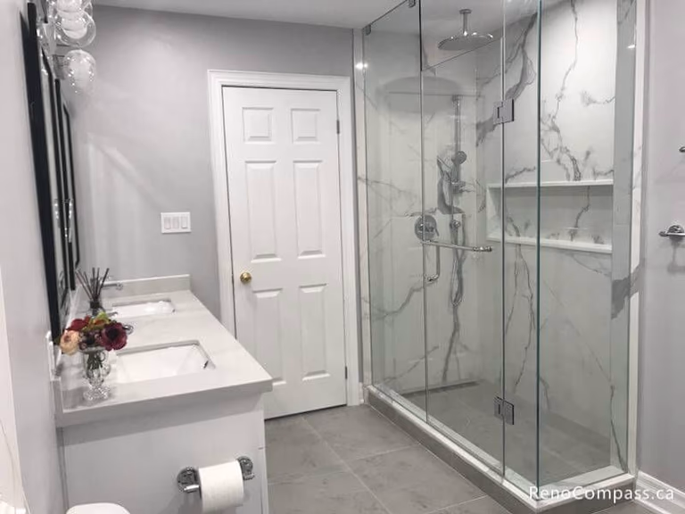 A spacious master bathroom renovation in Markham featuring a frameless glass shower with marble-style wall tiles and a contemporary white double vanity with quartz countertops.