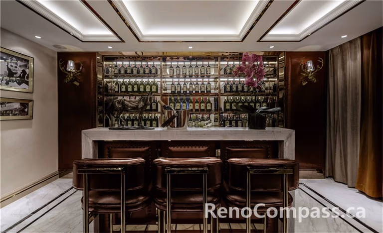 This Toronto interior renovation features a bespoke home bar design with a marble countertop, custom wood cabinetry, and a full-height illuminated wine and liquor display wall. Elegant ceiling lighting, brass accents, and tailored seating create a refined entertainment space perfect for hosting guests. Completed by an experienced Toronto Renovation Company, the project highlights premium finishes, functional layout planning, and sophisticated craftsmanship, delivering a private luxury bar experience within a modern residential setting.