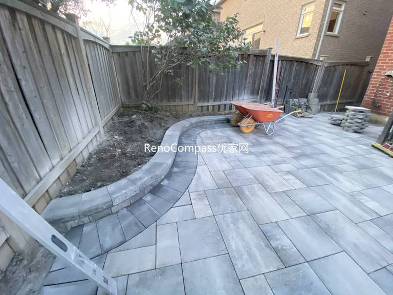 This Markham landscaping and interlocking project features a custom stone patio designed with a curved edge layout to soften the backyard space and improve flow. Large-format interlocking pavers were installed with precise alignment, creating a durable and visually balanced outdoor surface suitable for seating and everyday use. Integrated pathway lighting enhances safety and nighttime visibility, while the patio connects seamlessly with the existing wooden deck and side walkway. The combination of clean stone patterns and thoughtful layout delivers a functional, low-maintenance backyard upgrade completed by Reno Compass, serving homeowners in Markham and the surrounding GTA.