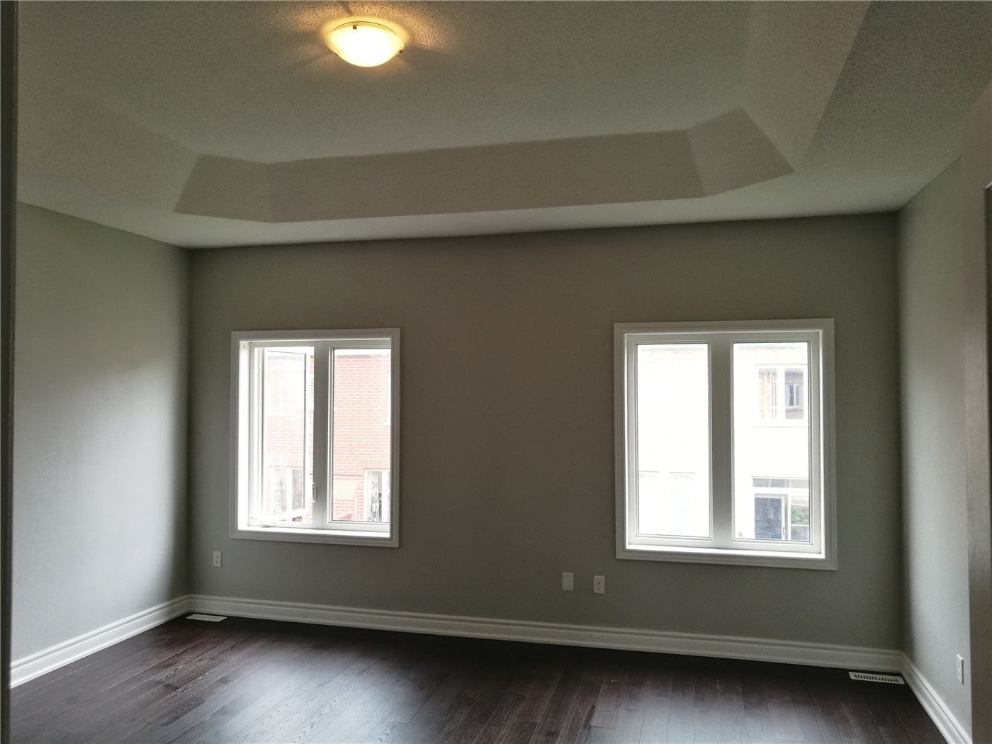 This image shows a bedroom after a Markham interior renovation, featuring a tray ceiling design, soft neutral wall colors, large windows for natural light, and dark hardwood flooring that creates a calm and balanced living environment.