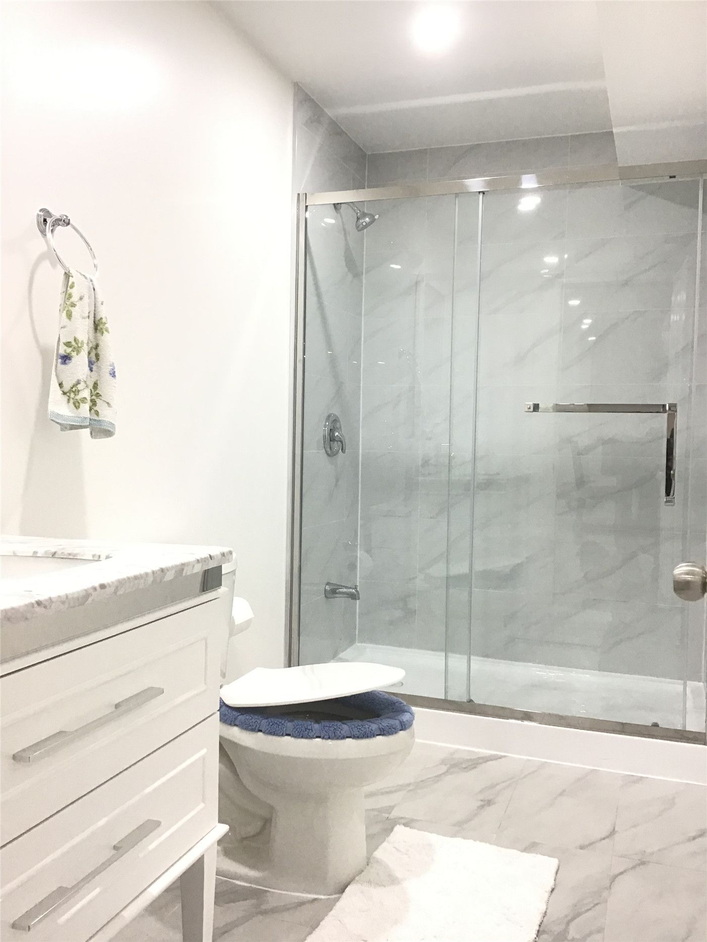 This Aurora basement renovation features a clean and modern bathroom design, including a frameless glass shower enclosure, marble-look wall tiles, and a sleek white vanity. The upgraded layout enhances both functionality and aesthetics, creating a bright and comfortable space in the finished basement.
