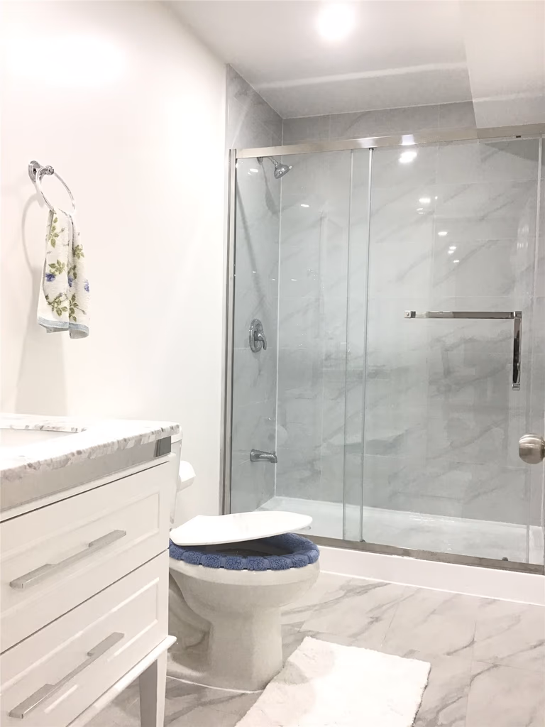 This Aurora basement renovation features a clean and modern bathroom design, including a frameless glass shower enclosure, marble-look wall tiles, and a sleek white vanity. The upgraded layout enhances both functionality and aesthetics, creating a bright and comfortable space in the finished basement.