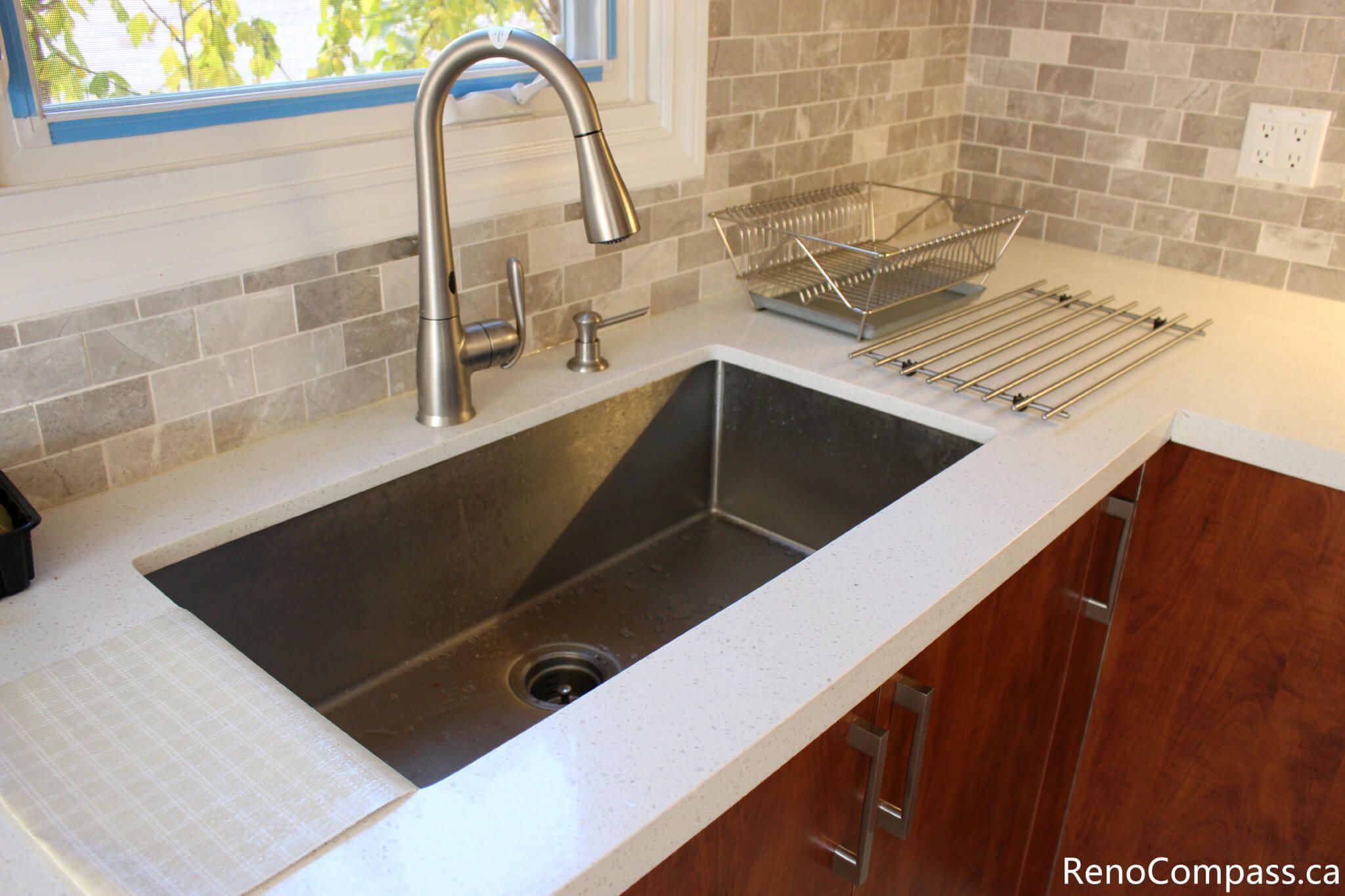 This close-up kitchen detail showcases a modern stainless steel undermount sink, sleek pull-down faucet, and durable quartz countertop installed as part of a full house renovation in Mississauga. The neutral mosaic backsplash and upgraded fixtures enhance both functionality and visual appeal, creating a clean and contemporary workspace. Completed by a professional Toronto renovation company, this renovation focuses on quality materials, practical design, and long-term everyday comfort for homeowners.