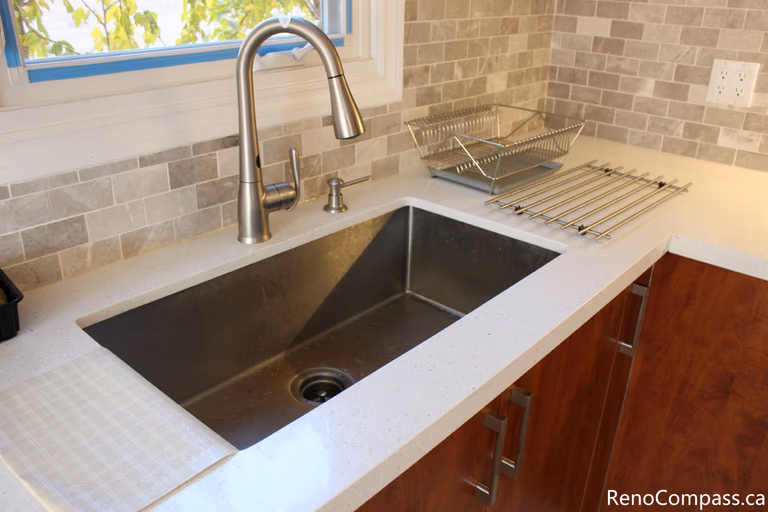 This close-up kitchen detail showcases a modern stainless steel undermount sink, sleek pull-down faucet, and durable quartz countertop installed as part of a full house renovation in Mississauga. The neutral mosaic backsplash and upgraded fixtures enhance both functionality and visual appeal, creating a clean and contemporary workspace. Completed by a professional Toronto renovation company, this renovation focuses on quality materials, practical design, and long-term everyday comfort for homeowners.