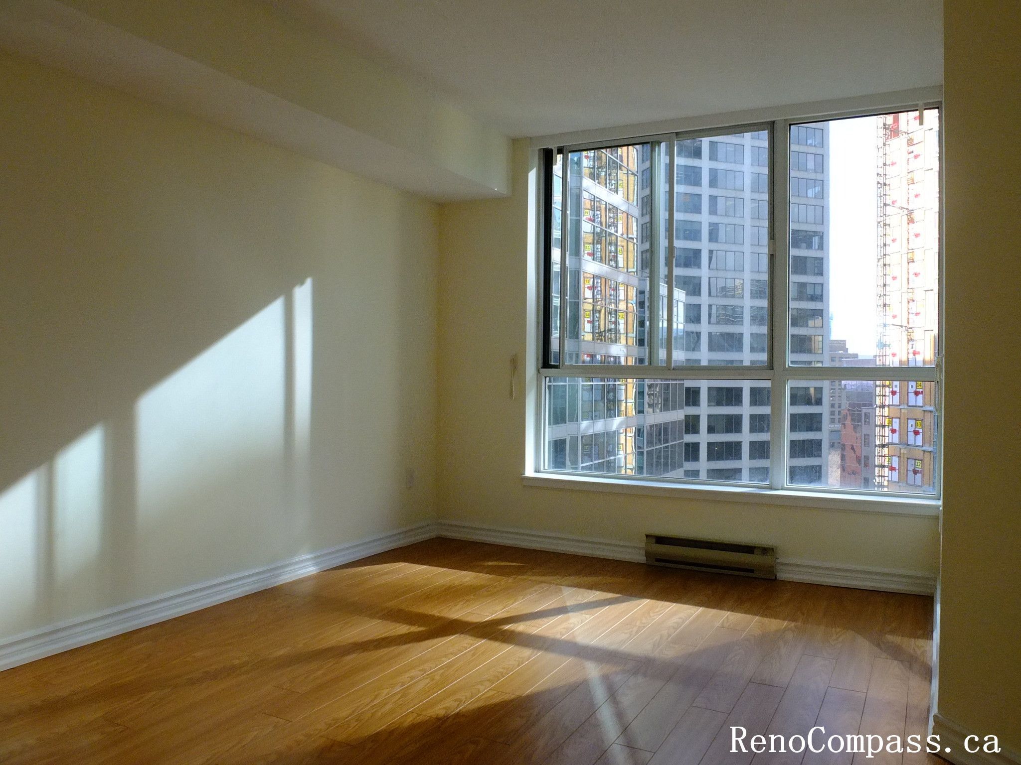 This image shows a bright bedroom in a Toronto condominium before renovation, featuring hardwood flooring and a large window with city views that brings in abundant natural light. As part of a Toronto interior renovation project, the space was prepared for upgrades to improve layout, finishes, and overall modern living comfort.