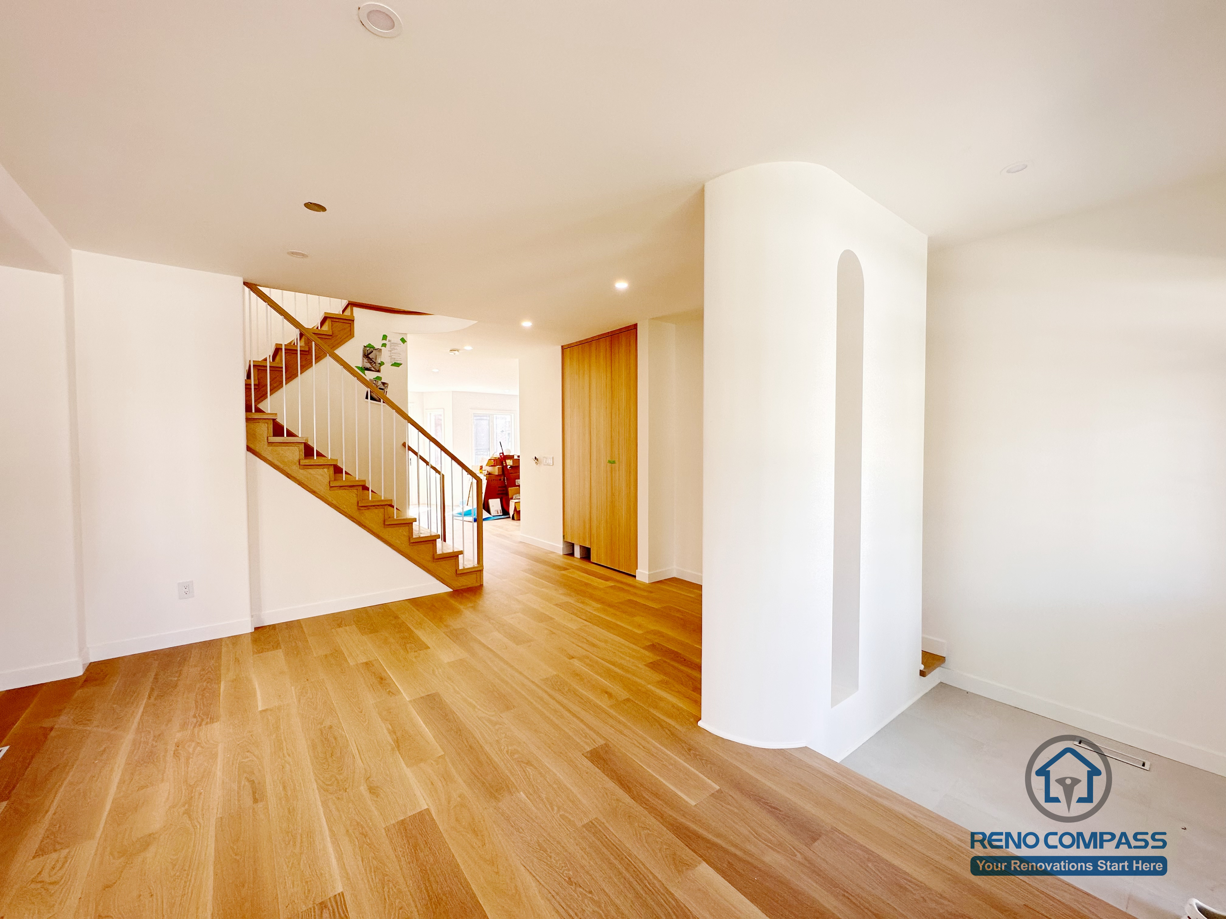 This image highlights a Markham flooring and staircase renovation featuring continuous hardwood flooring and a clean transition between the living area and stairway. The open layout, rounded architectural column, and natural wood stair treads create a smooth visual flow while maintaining clear spatial separation. Recessed lighting enhances brightness without overpowering the space. Completed by a professional Toronto renovation company, Reno Compass Inc., this project demonstrates careful attention to flooring alignment, staircase detailing, and long-term durability.