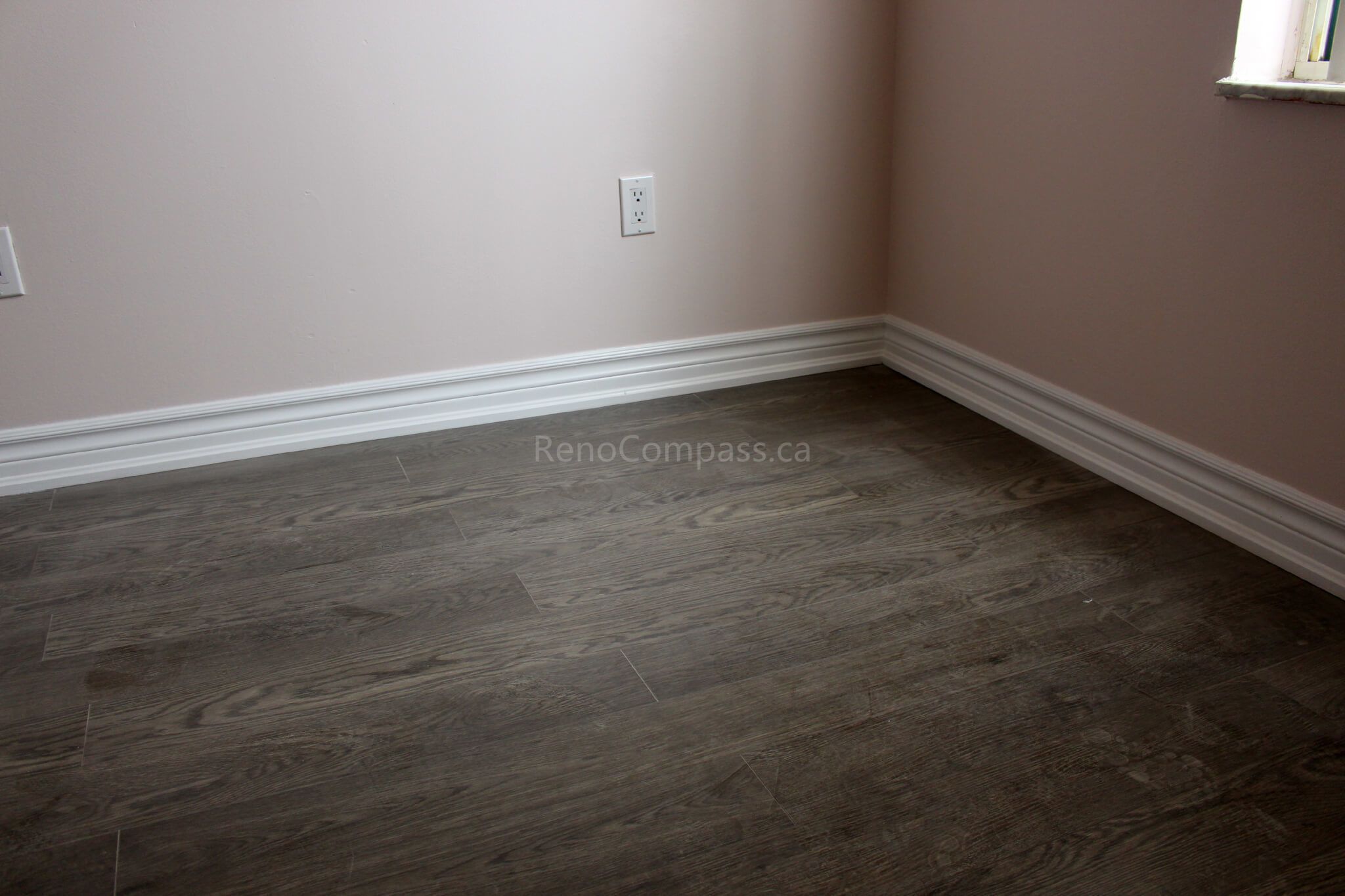 Newly installed dark wood-look luxury vinyl flooring with crisp white baseboards, enhancing the elegance of this Mississauga home renovation. The modern flooring finish blends durability and style, ideal for contemporary interiors.