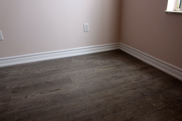 Newly installed dark wood-look luxury vinyl flooring with crisp white baseboards, enhancing the elegance of this Mississauga home renovation. The modern flooring finish blends durability and style, ideal for contemporary interiors.