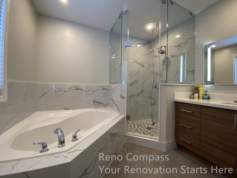 This Newmarket bathroom renovation features a well-coordinated layout combining a built-in bathtub, a frameless glass shower enclosure, and a modern vanity with clean-lined storage. Marble-look wall tiles extend around the tub and shower area, creating a seamless visual connection while enhancing durability and moisture resistance. The transparent glass shower enclosure preserves openness and allows light to circulate throughout the space, making the bathroom feel brighter and more spacious. Neutral finishes and carefully selected fixtures contribute to a calm, spa-inspired atmosphere designed for everyday comfort and long-term use. This renovation was completed by Reno Compass, serving homeowners in Newmarket and across the GTA.