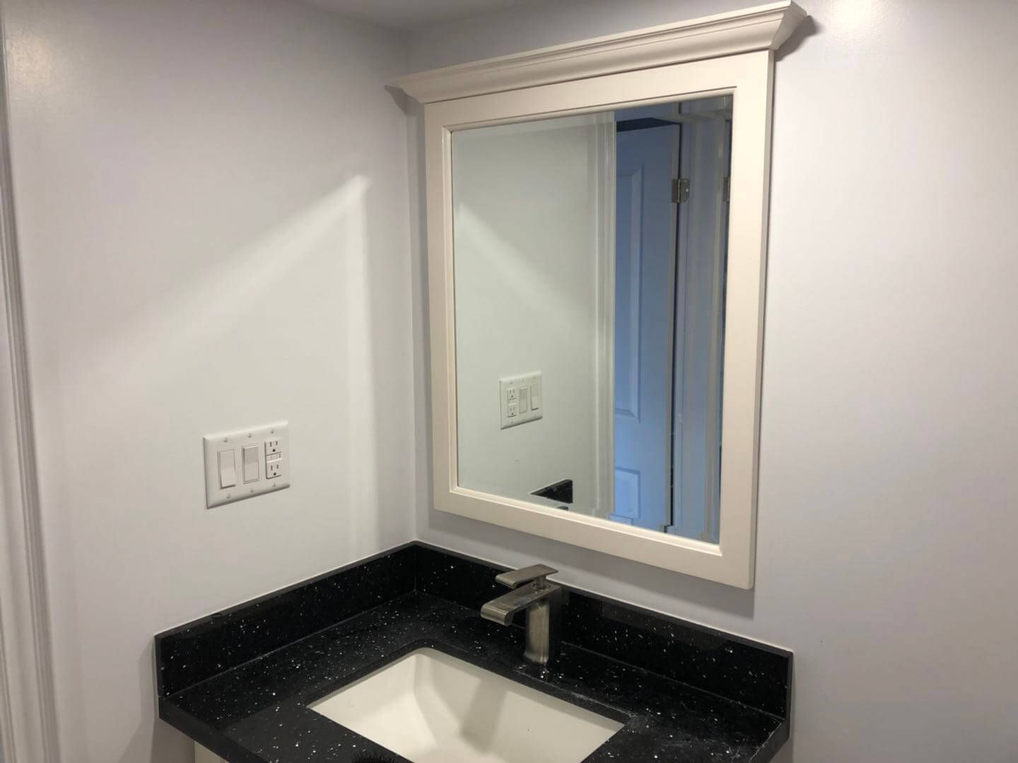 Custom bathroom vanity installation in a Toronto basement renovation, featuring a black quartz countertop, undermount sink, chrome single-handle faucet, framed mirror, and clean white wall finish for a bright and functional lower-level bathroom space.