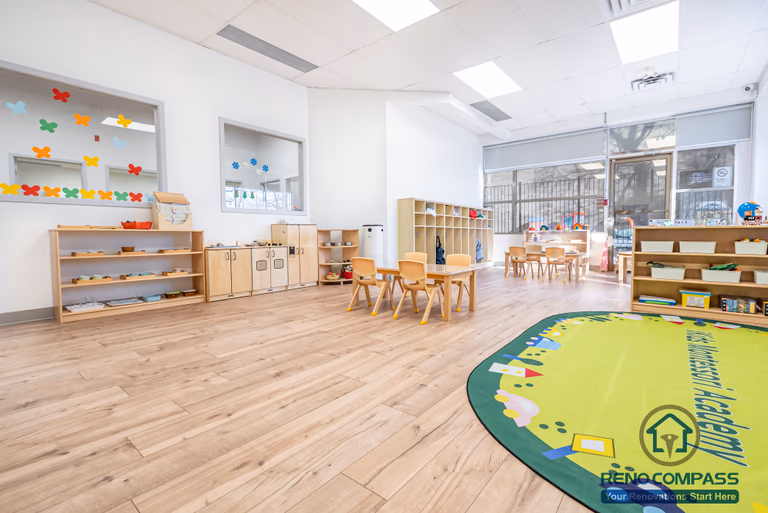 This Markham daycare renovation features a spacious open classroom designed to support multiple learning and play activities within a safe and well-organized environment. The layout provides clear sightlines for supervision while allowing children to move freely between learning tables, storage areas, and soft play zones. Low-height shelving and child-accessible storage promote independence and daily organization. Durable, easy-to-clean flooring and bright overhead lighting enhance safety, comfort, and long-term maintenance. Completed by a Toronto renovation company, Reno Compass Inc., this daycare interior renovation reflects a thoughtful approach to space planning, safety compliance, and functional design for modern childcare facilities.